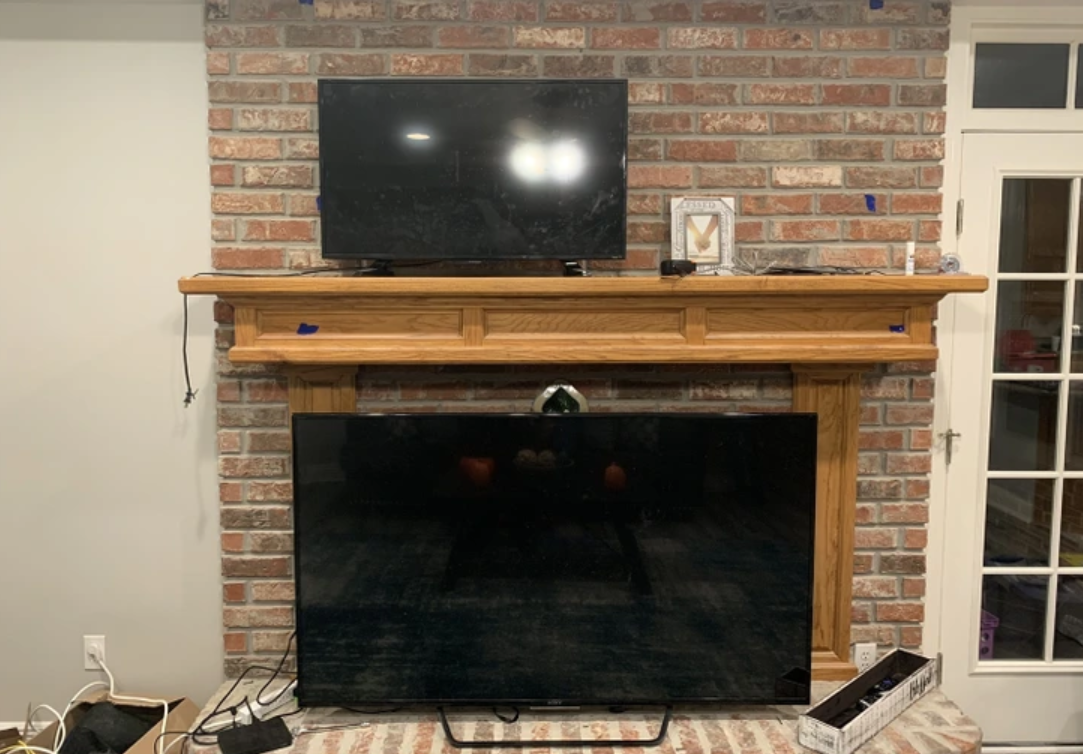 Living room fireplace with brick surround, wooden mantel, wall-mounted TV, and glass cabinet to the right