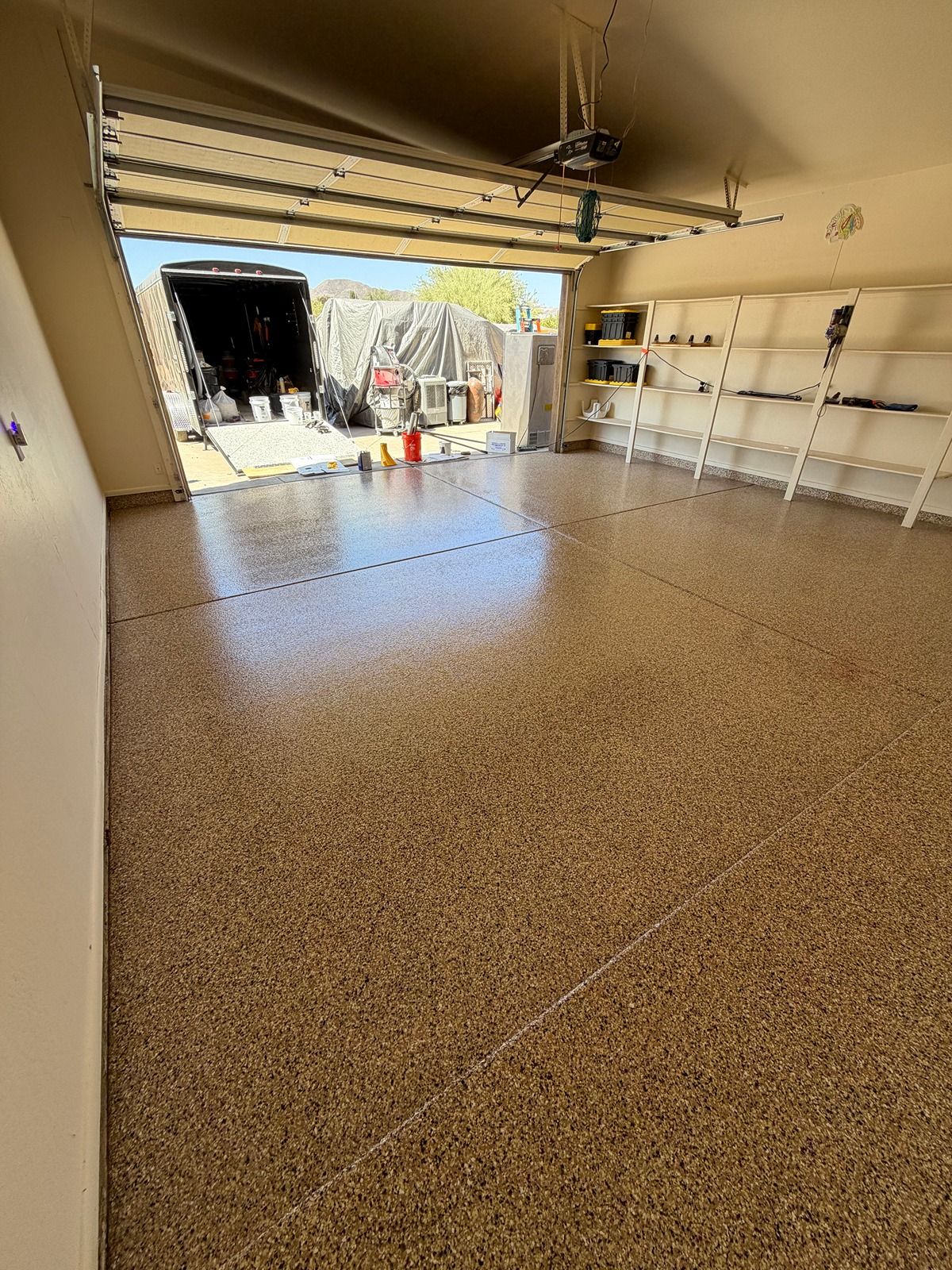 Empty garage with speckled floor, open door, and shelves along the right wall