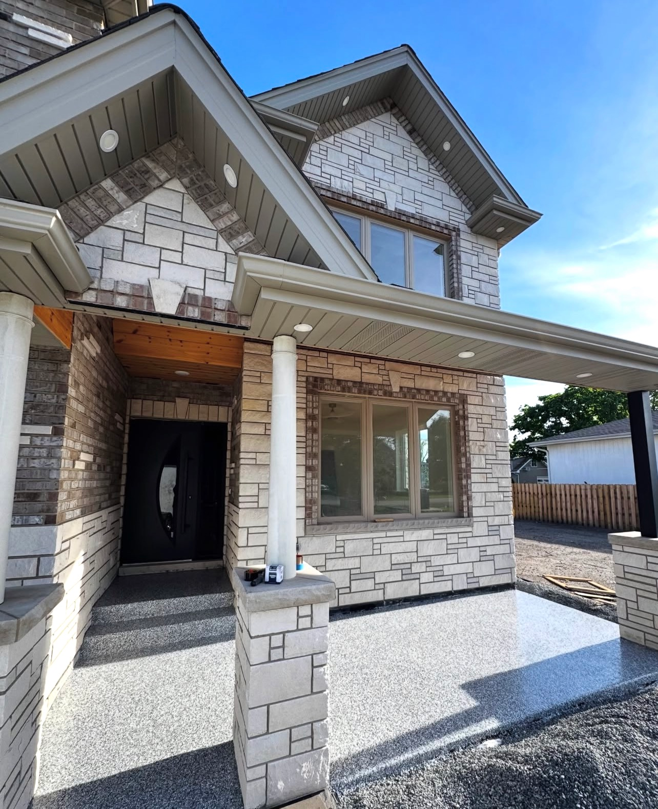 Modern two-story stone house with a covered front porch, large windows, and blue sky above.
