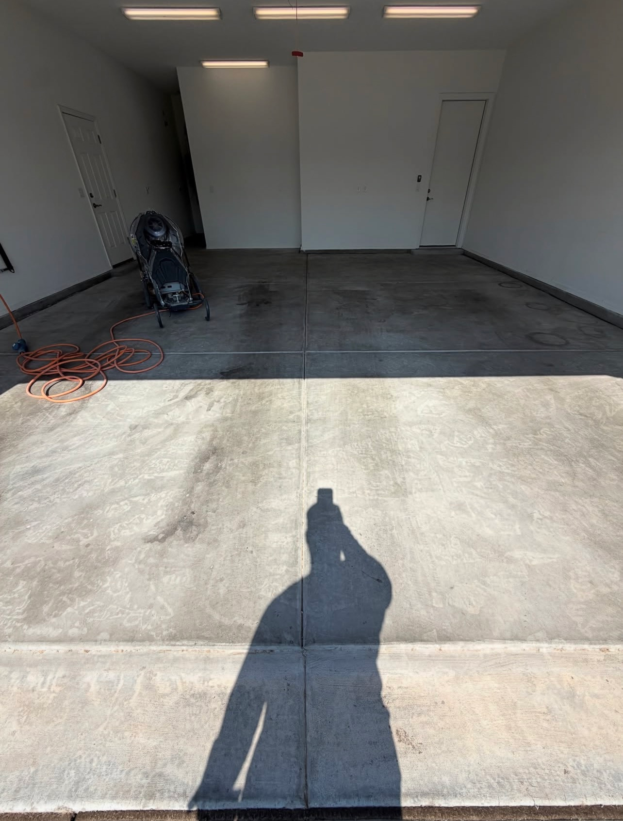 Empty garage with a concrete floor, white walls, and a person’s shadow in the foreground.