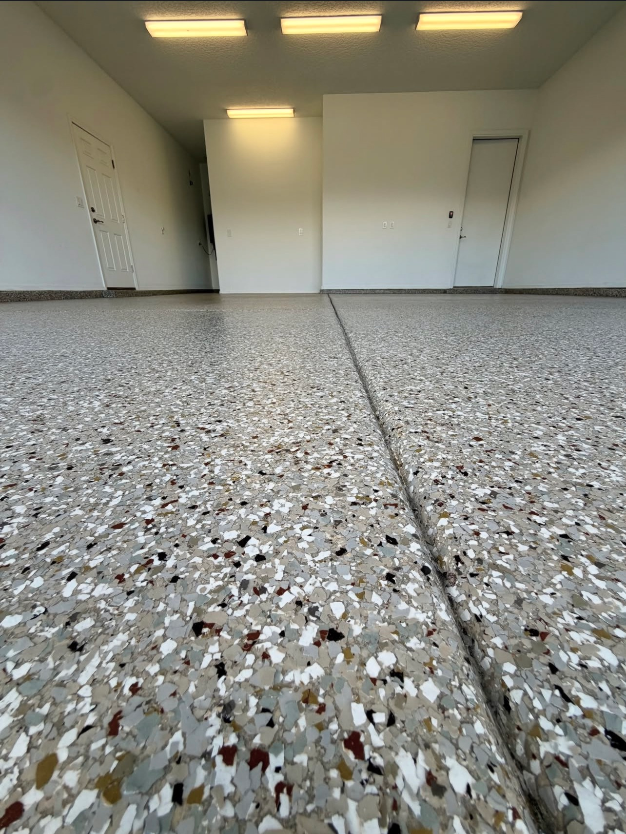 Empty garage with gray speckled floor, white walls, and overhead lights