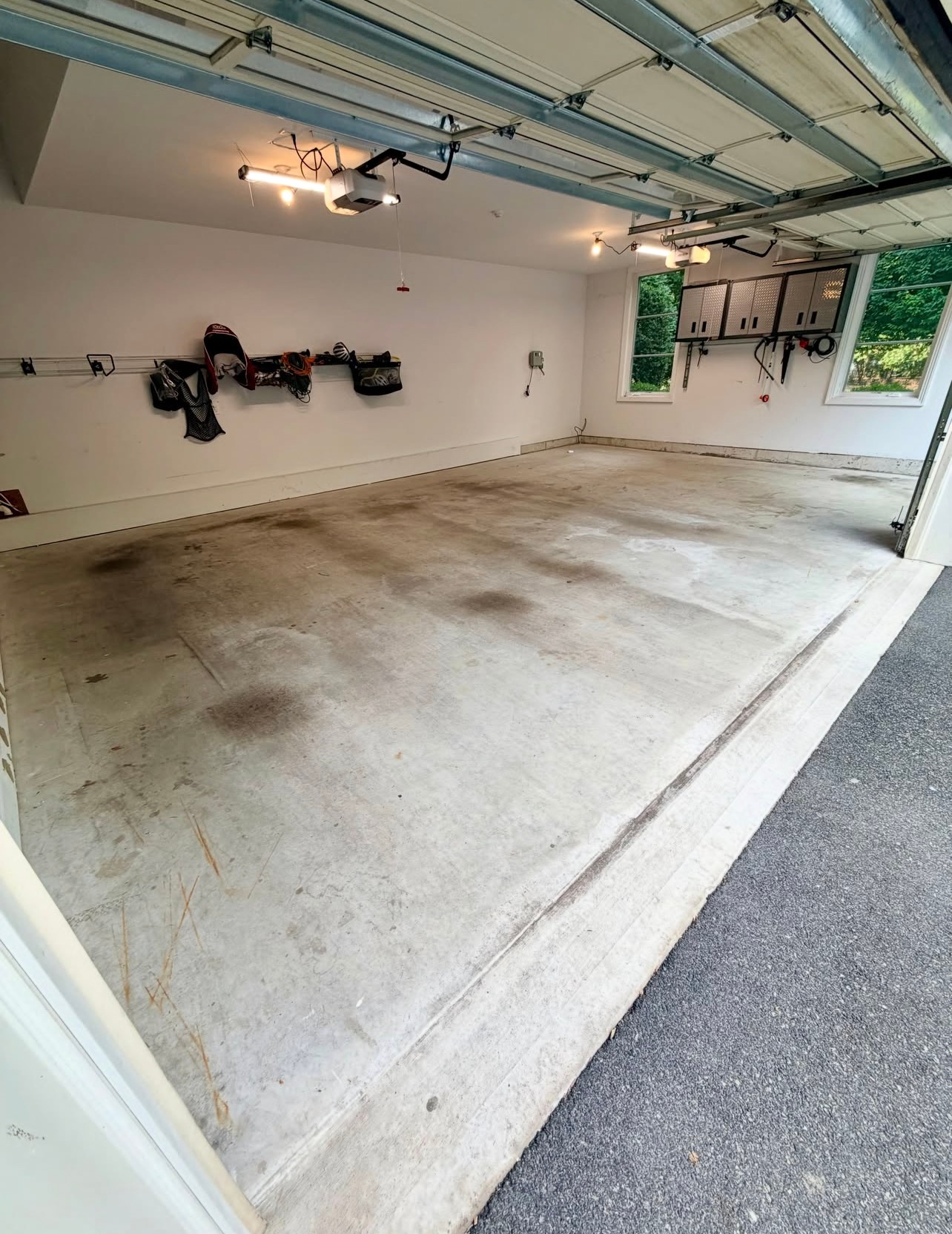 Empty residential garage with concrete floor, open door, ceiling lights, and a wall-mounted bicycle rack.