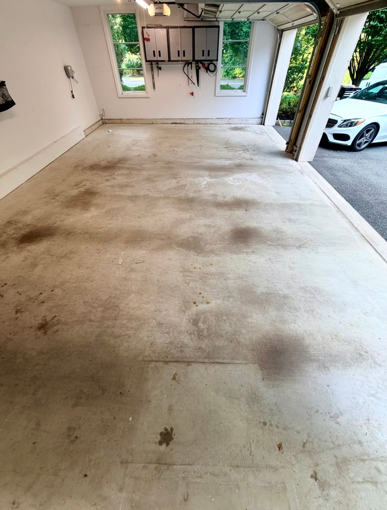 Empty garage with stained concrete floor and white walls, open to driveway with a white car outside.