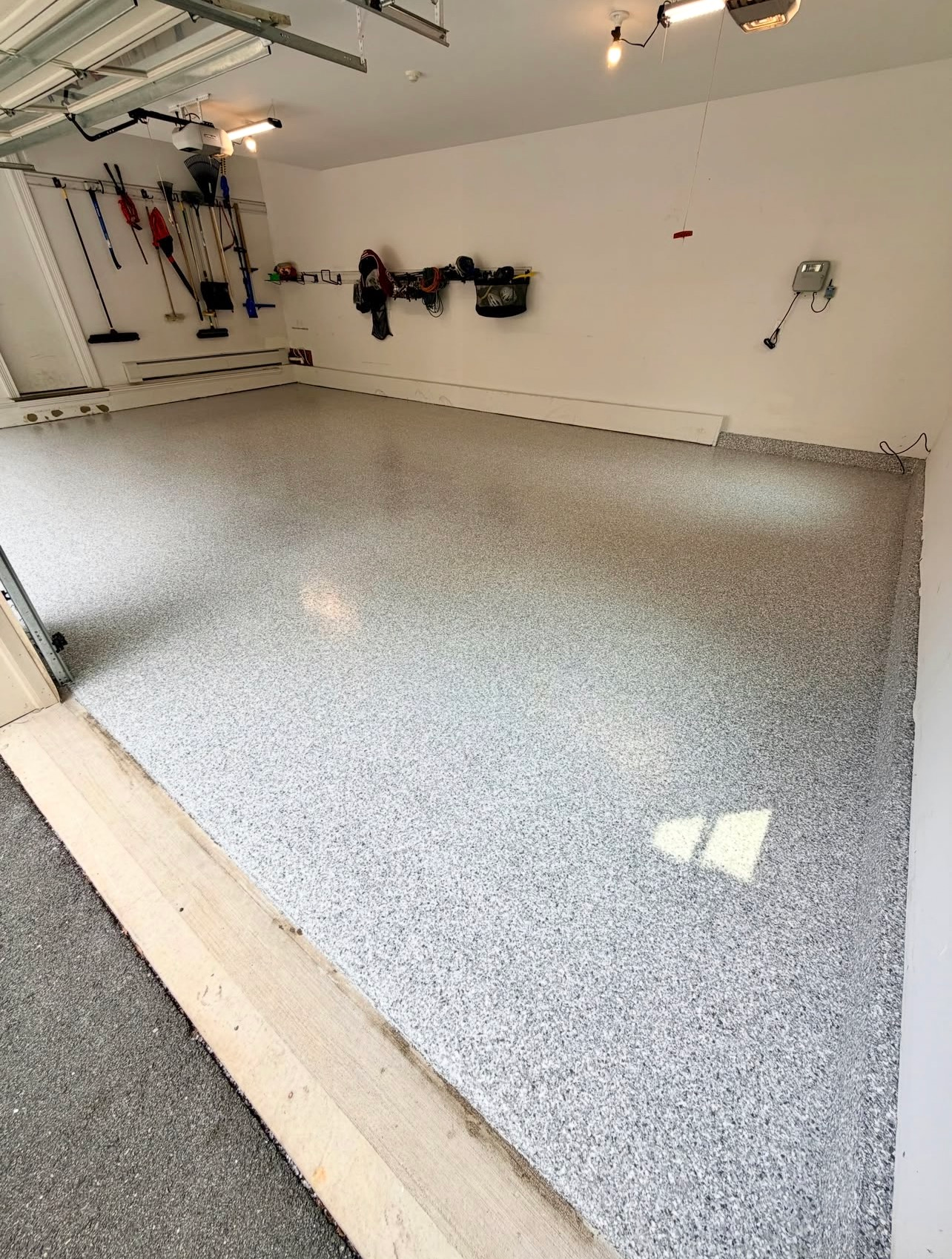 Empty garage with a gray speckled epoxy floor and white walls, lit by overhead lights.