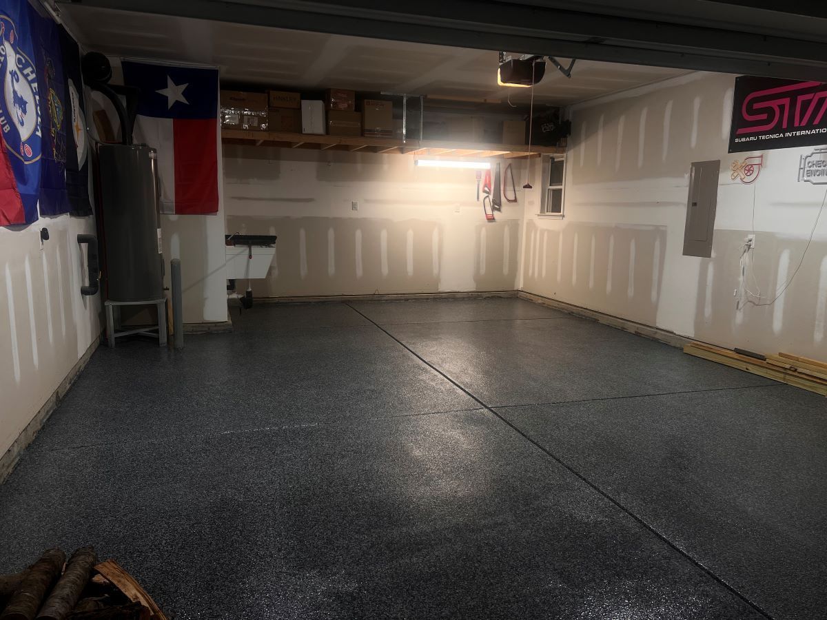 Empty garage interior with unfinished walls, speckled floor, and a bright light at the back.