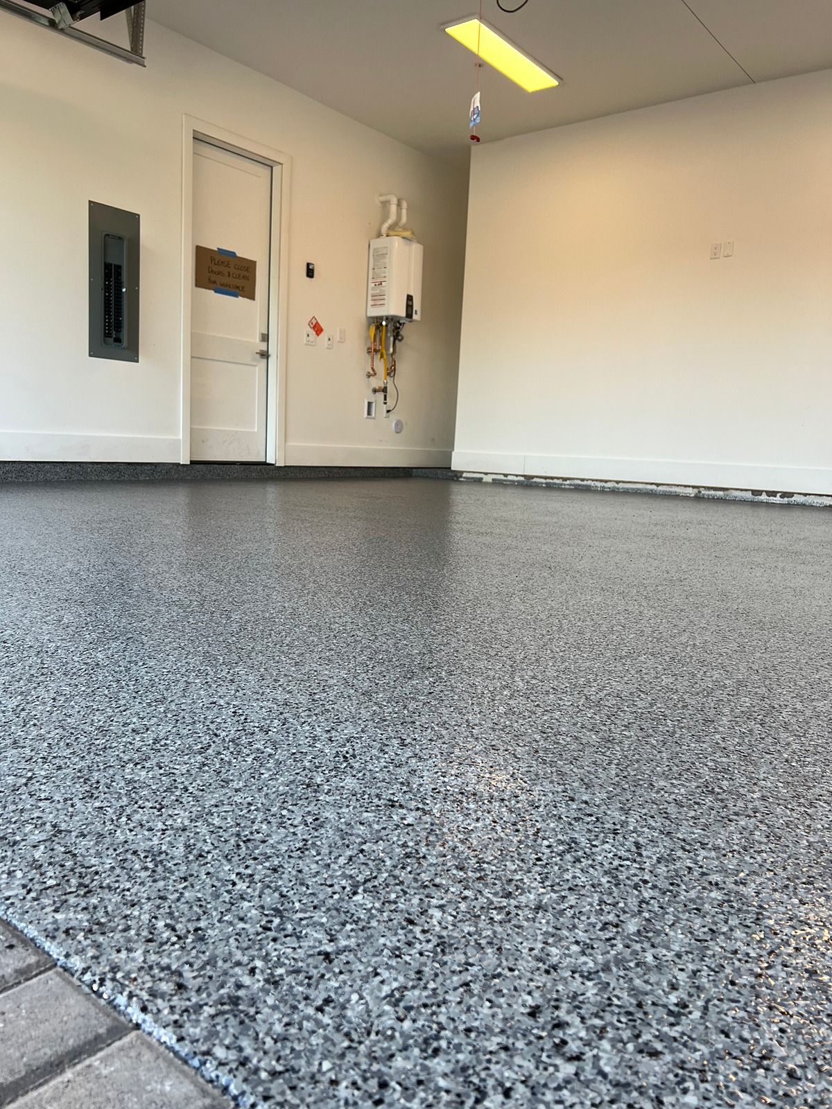 Empty garage with speckled gray floor, white walls, and a closed door on the left.