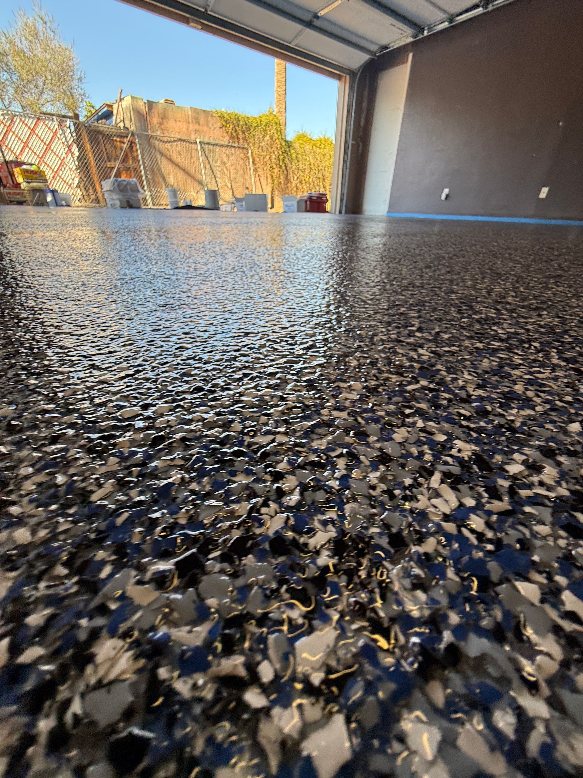 Low-angle view of a glossy speckled floor inside a covered garage, with bright daylight in the background