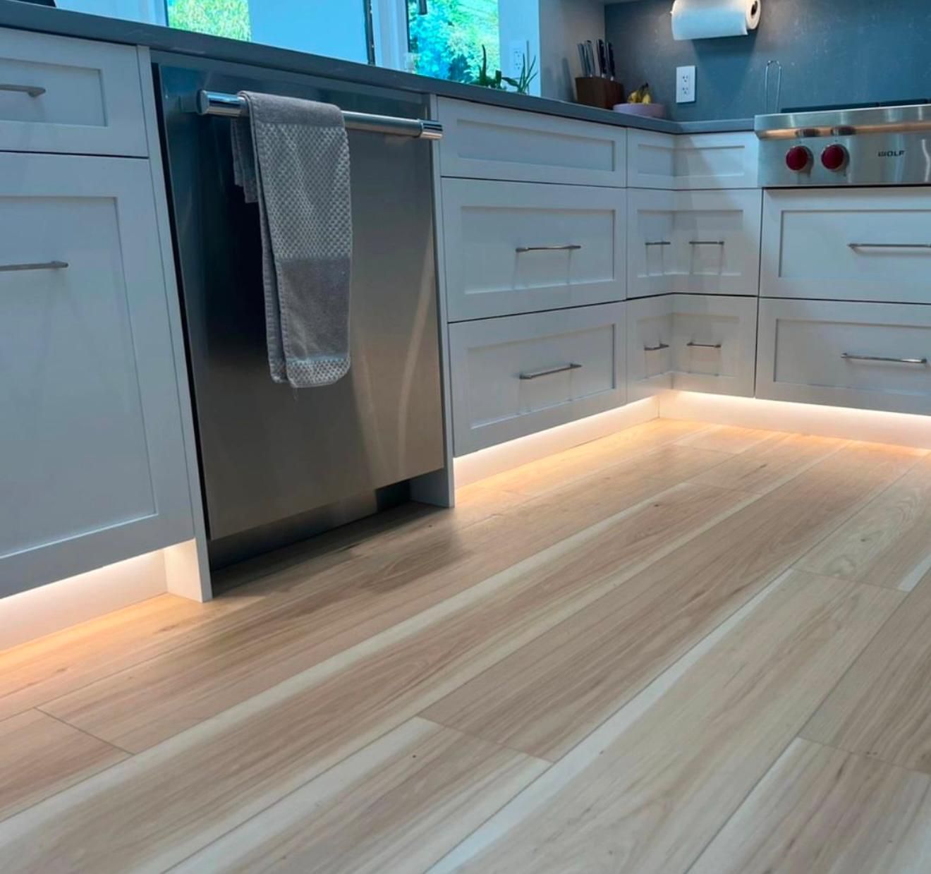 Modern kitchen with white cabinets, stainless dishwasher, and warm under-cabinet floor lighting