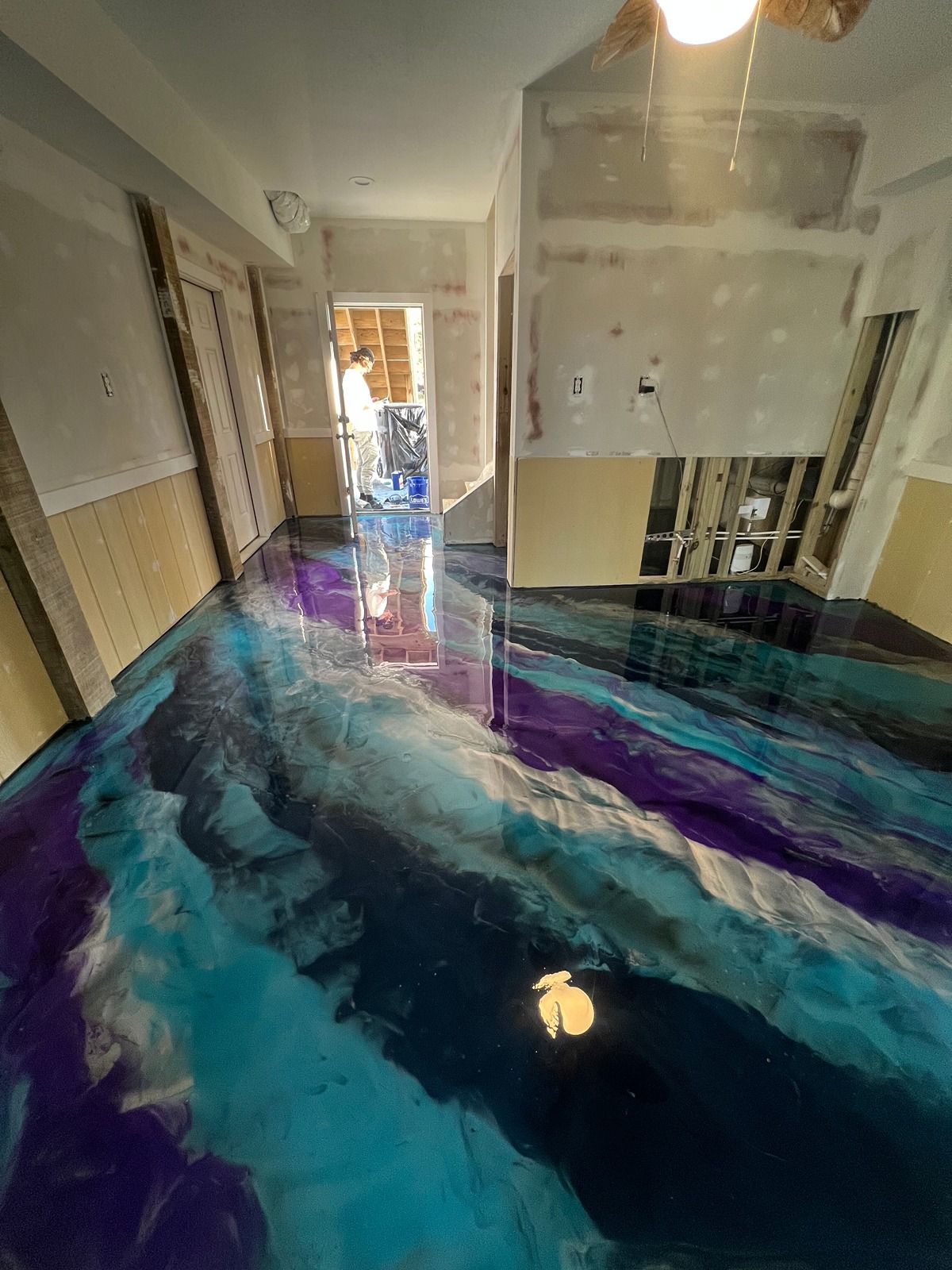 Hallway floor covered in swirling blue and purple water-like artwork, viewed toward an open doorway