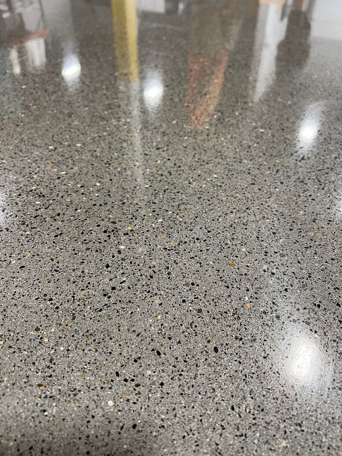 Speckled gray polished floor reflecting overhead lights and blurred objects