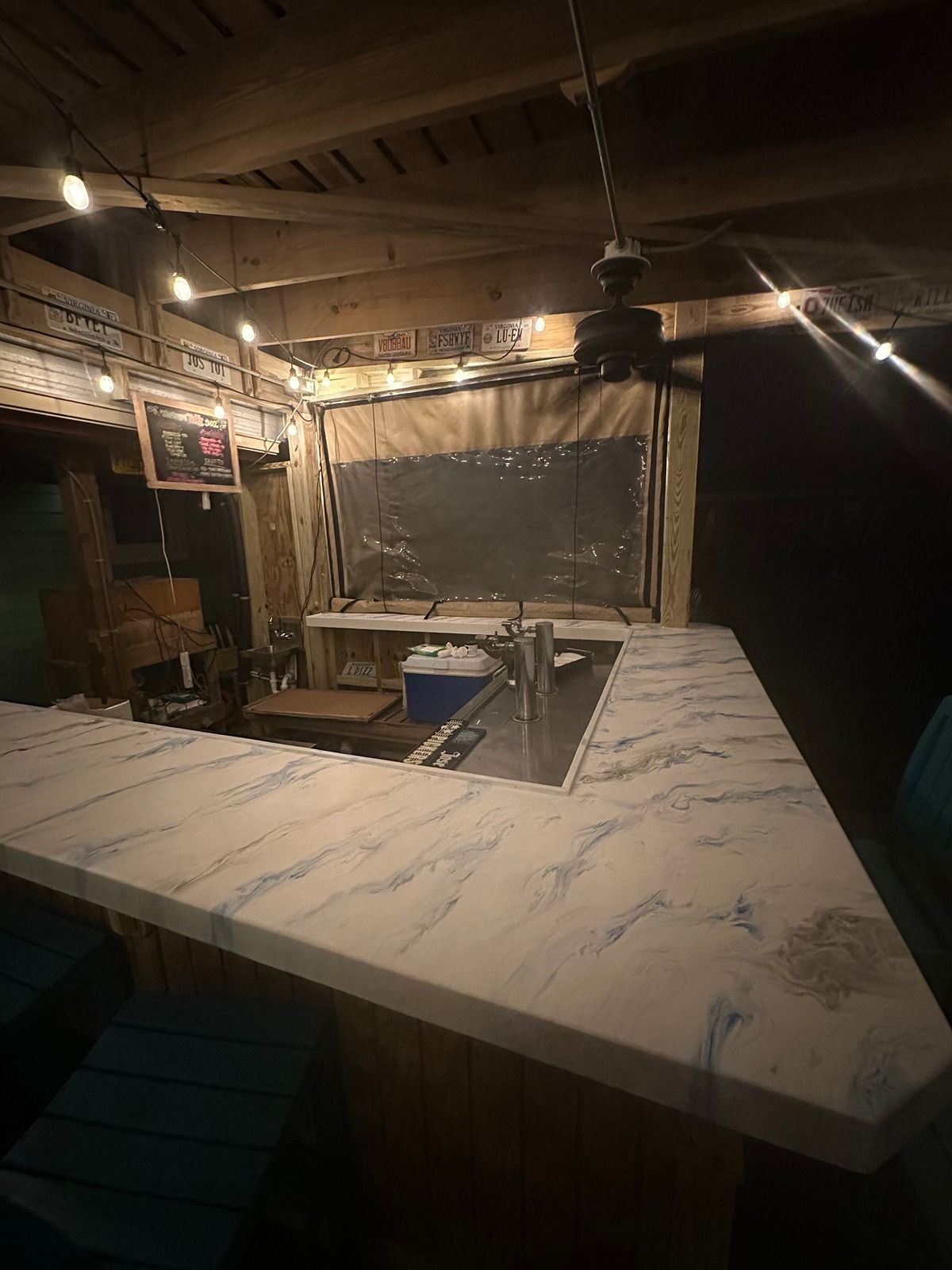 Dimly lit outdoor bar with a white marble counter and a small sink under a thatched roof.