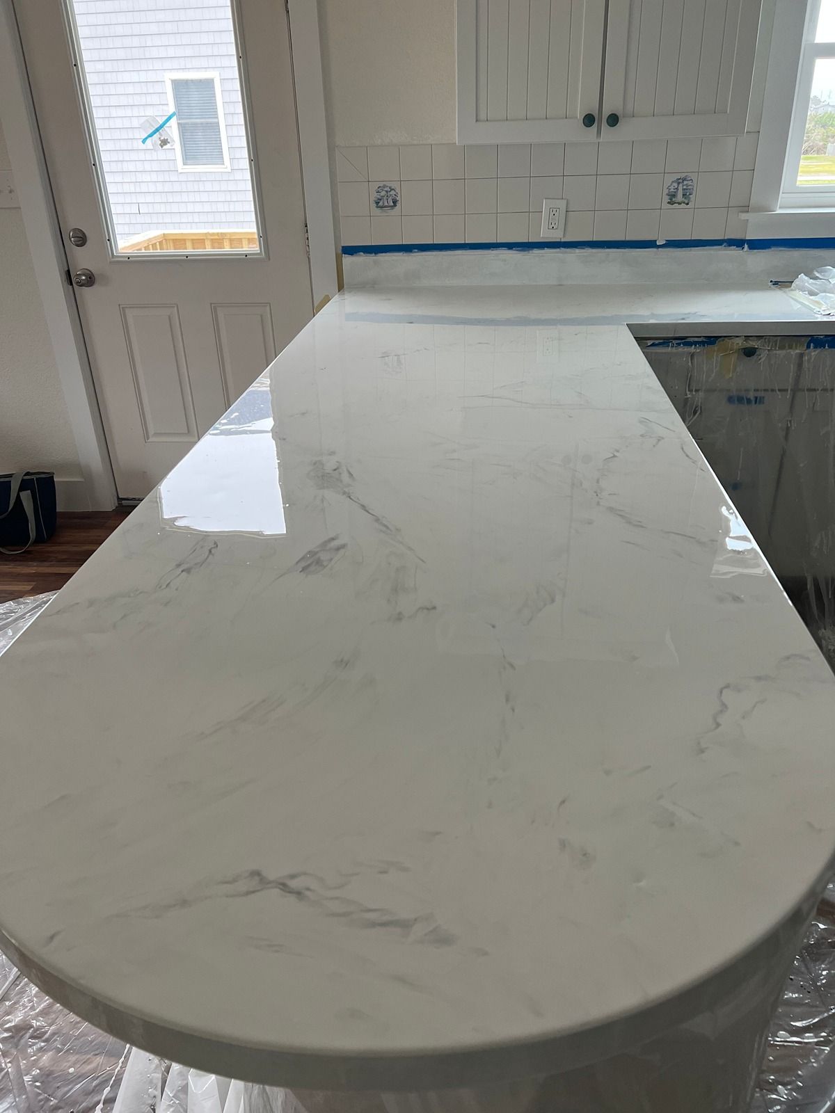 Kitchen island with white marble-look countertop and rounded end, in a bright kitchen with white cabinets and a door.
