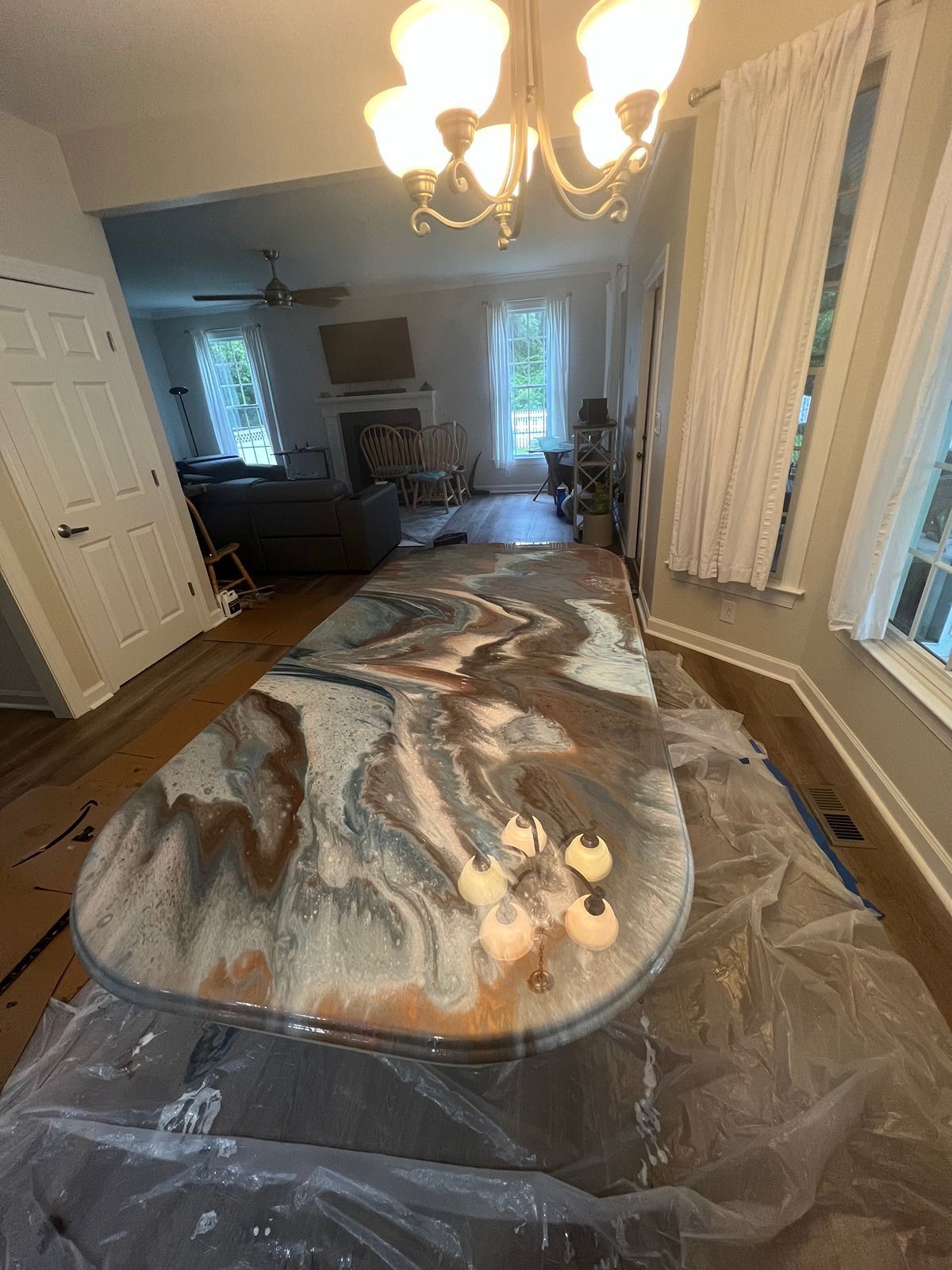 Modern living room with a large resin table on plastic sheeting and curtains by the windows