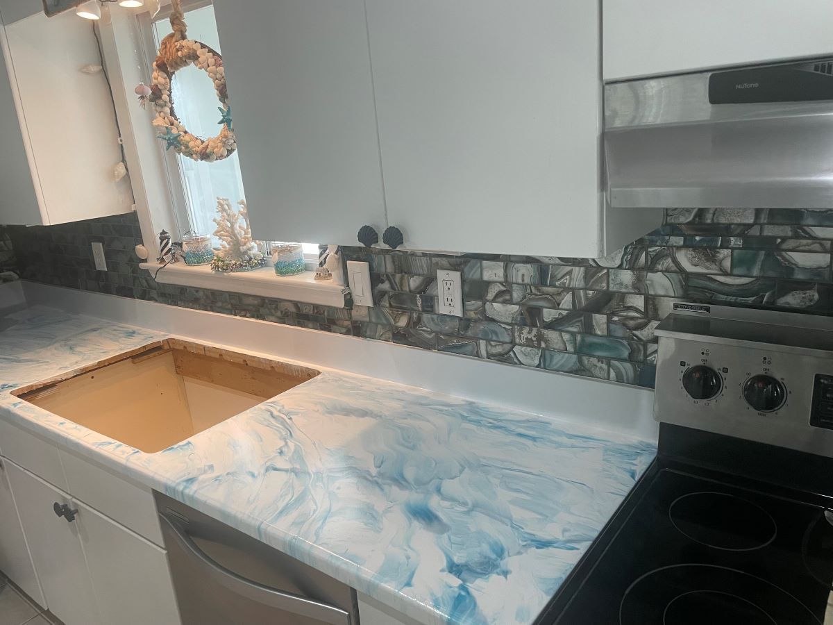 Kitchen with marble-look countertop, undermount sink cutout, gray cabinets, and tile backsplash near a window.