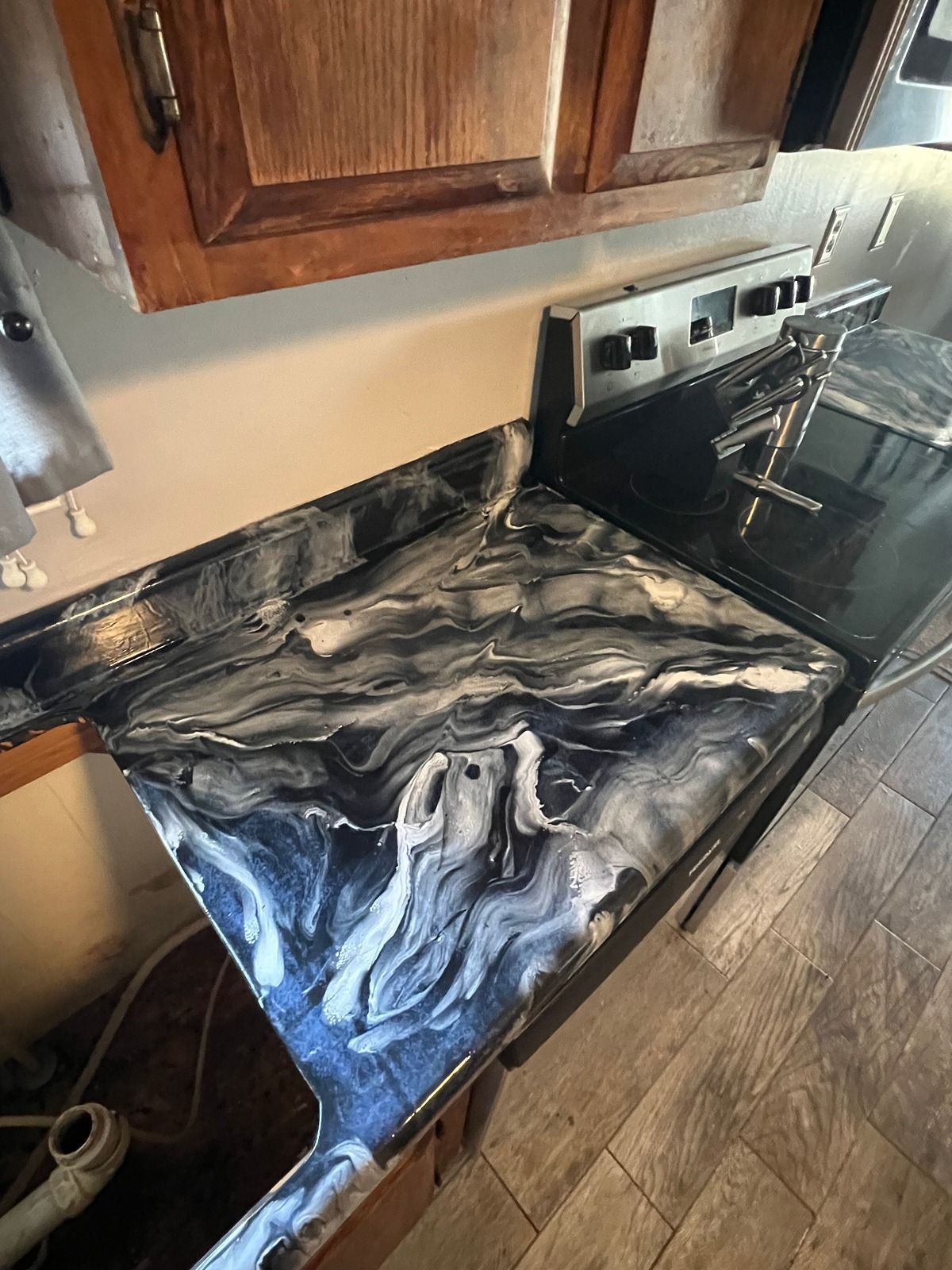 Kitchen countertop with a black-and-white marbled epoxy finish beside a stove and wooden cabinets