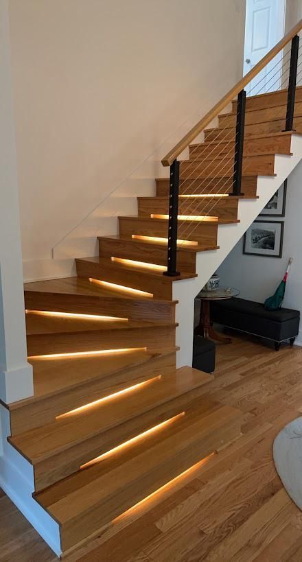 Indoor wooden staircase with a black railing and sunlight streaming through the steps