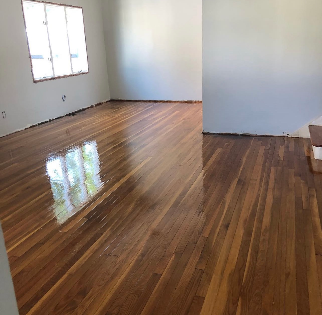 Empty room with polished wooden floors, white walls, and a window letting in daylight