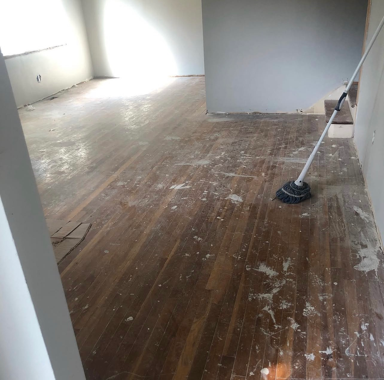 Dusty empty room with worn wood floors being cleaned with a mop or broom
