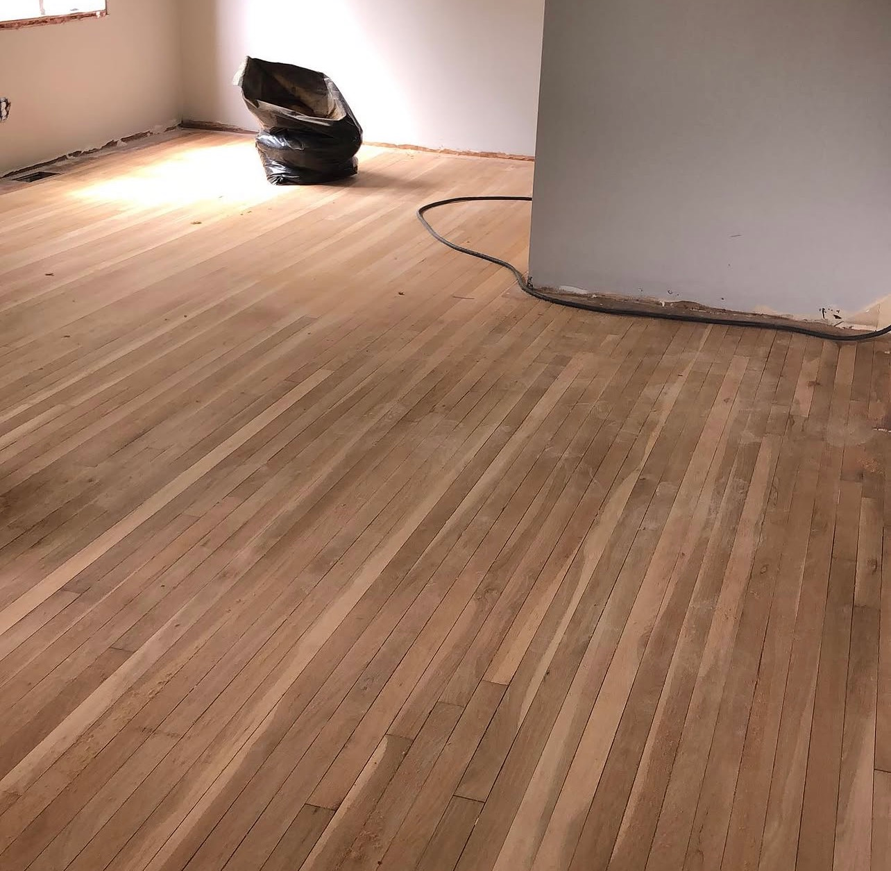 Empty room with newly sanded wood floor and a black bag near the wall.