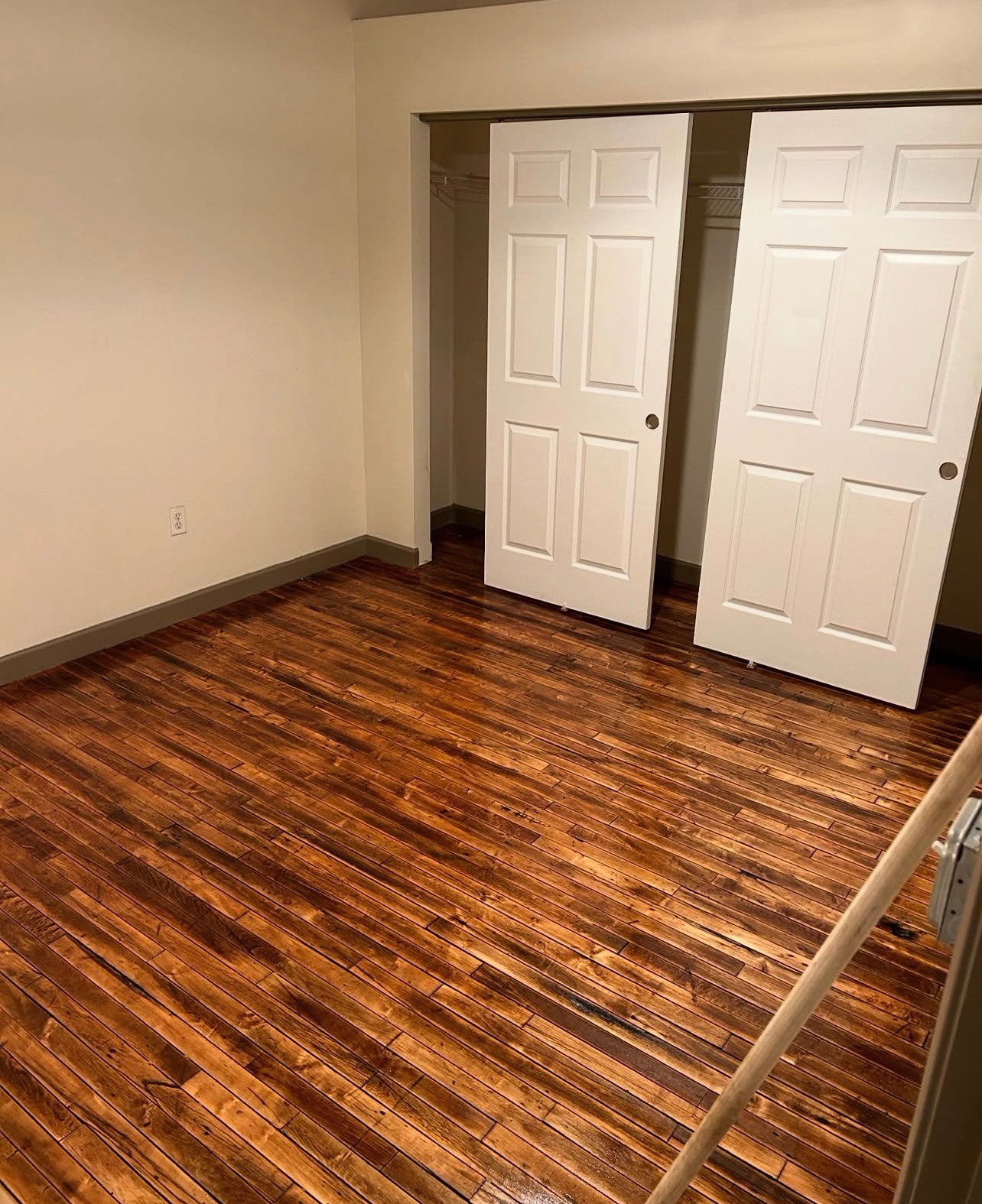Empty room with wood floor, white closet doors, and a stair railing in the foreground.
