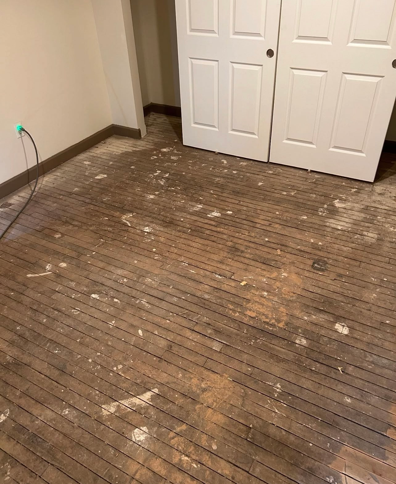 Damaged hardwood floor with scattered debris in a room near white double doors