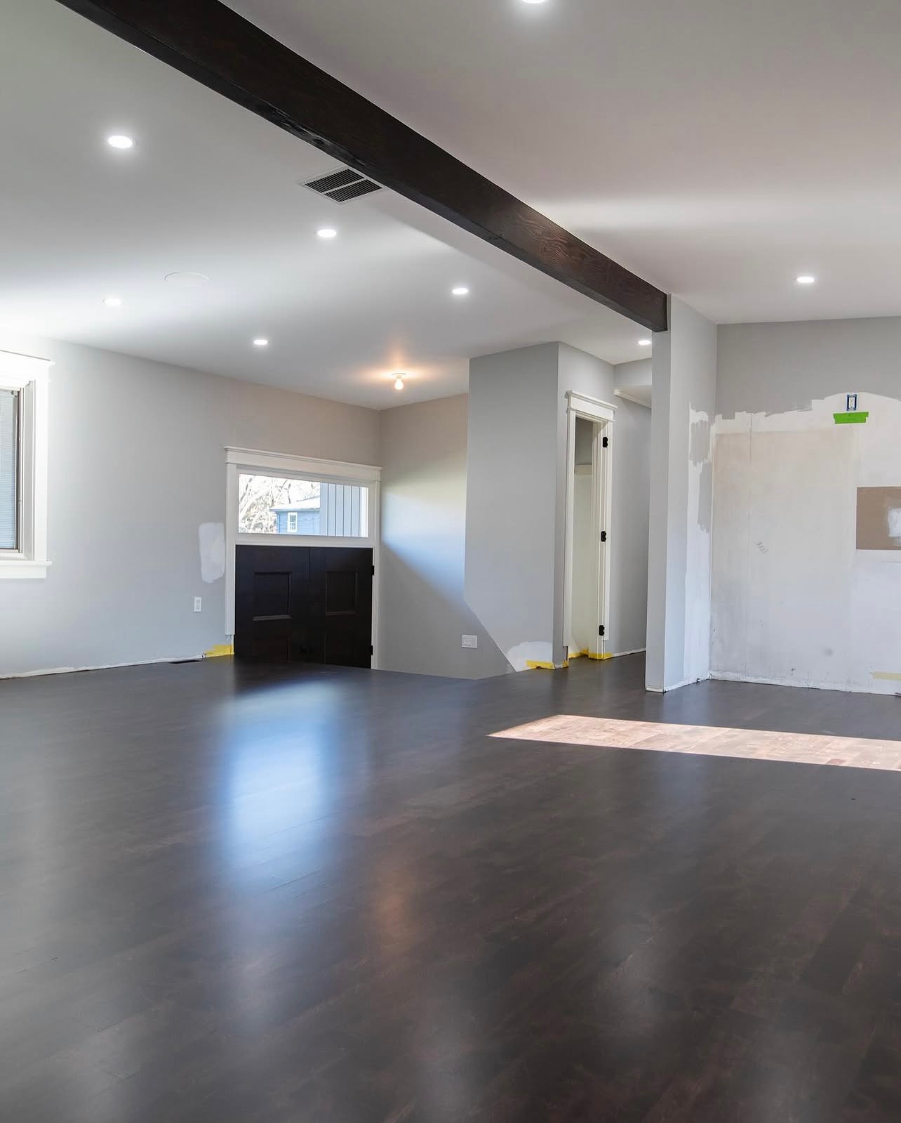 Empty modern living room with dark wood floors, white walls, recessed lights, and a doorway to another room