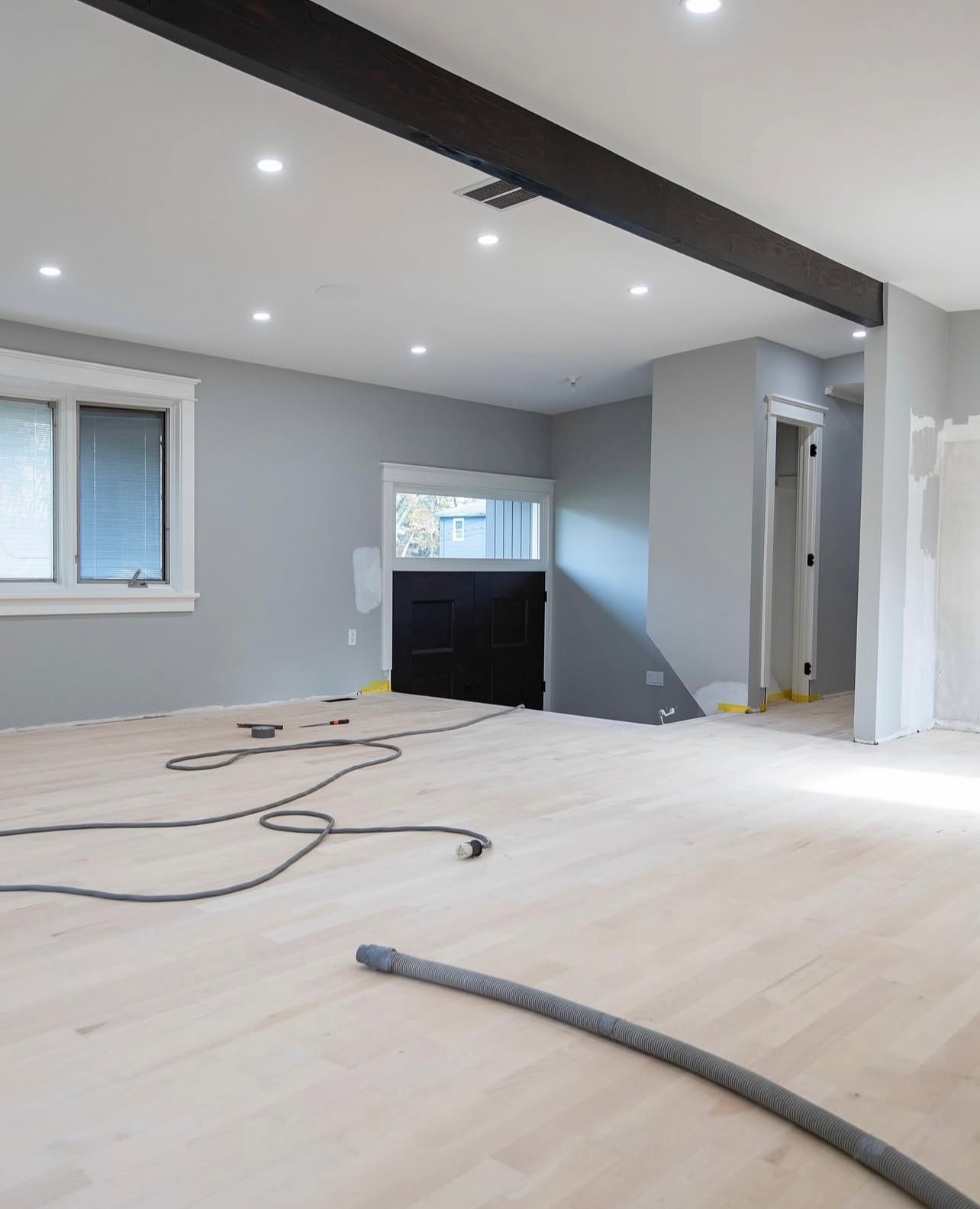 Bright unfinished room with light wood floor, gray walls, recessed lights, and loose cables on the floor.