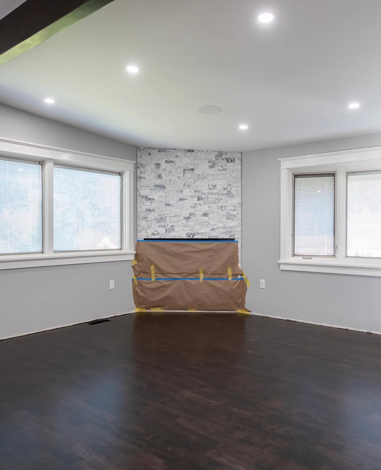 Empty room with dark wood floors, white walls, recessed lights, and a covered fireplace on the back wall.