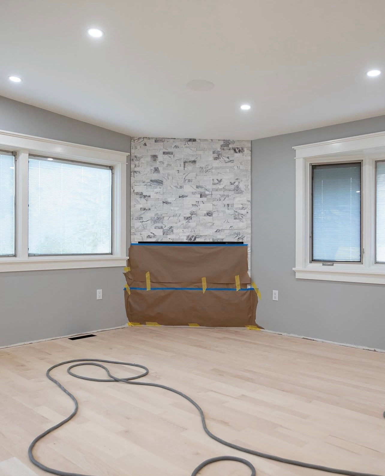 Empty room with light wood floor, white walls, two windows, and a covered fireplace or wall panel.