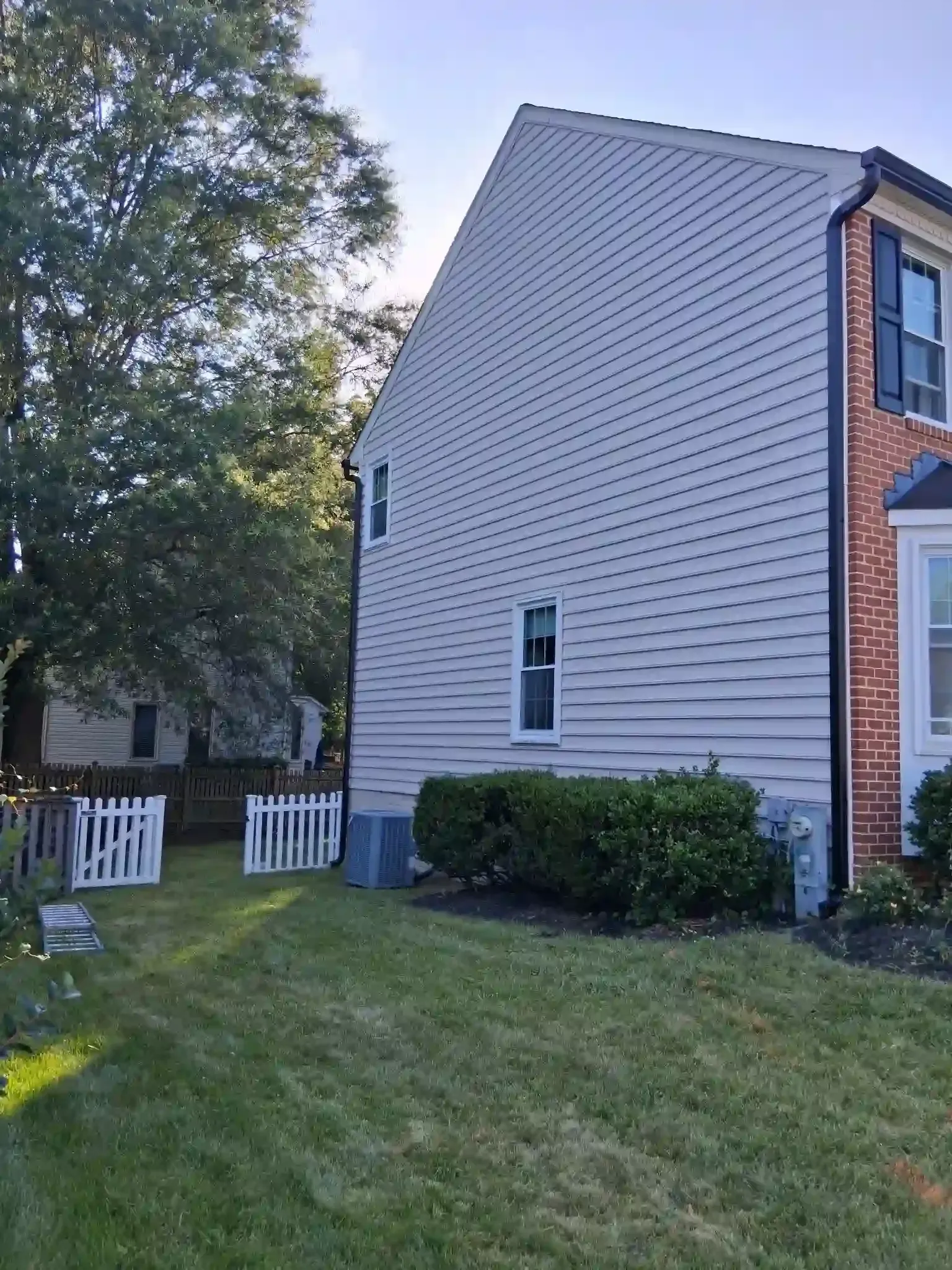 Side view of a white townhouse with shrubs, lawn, and a small white fence under trees