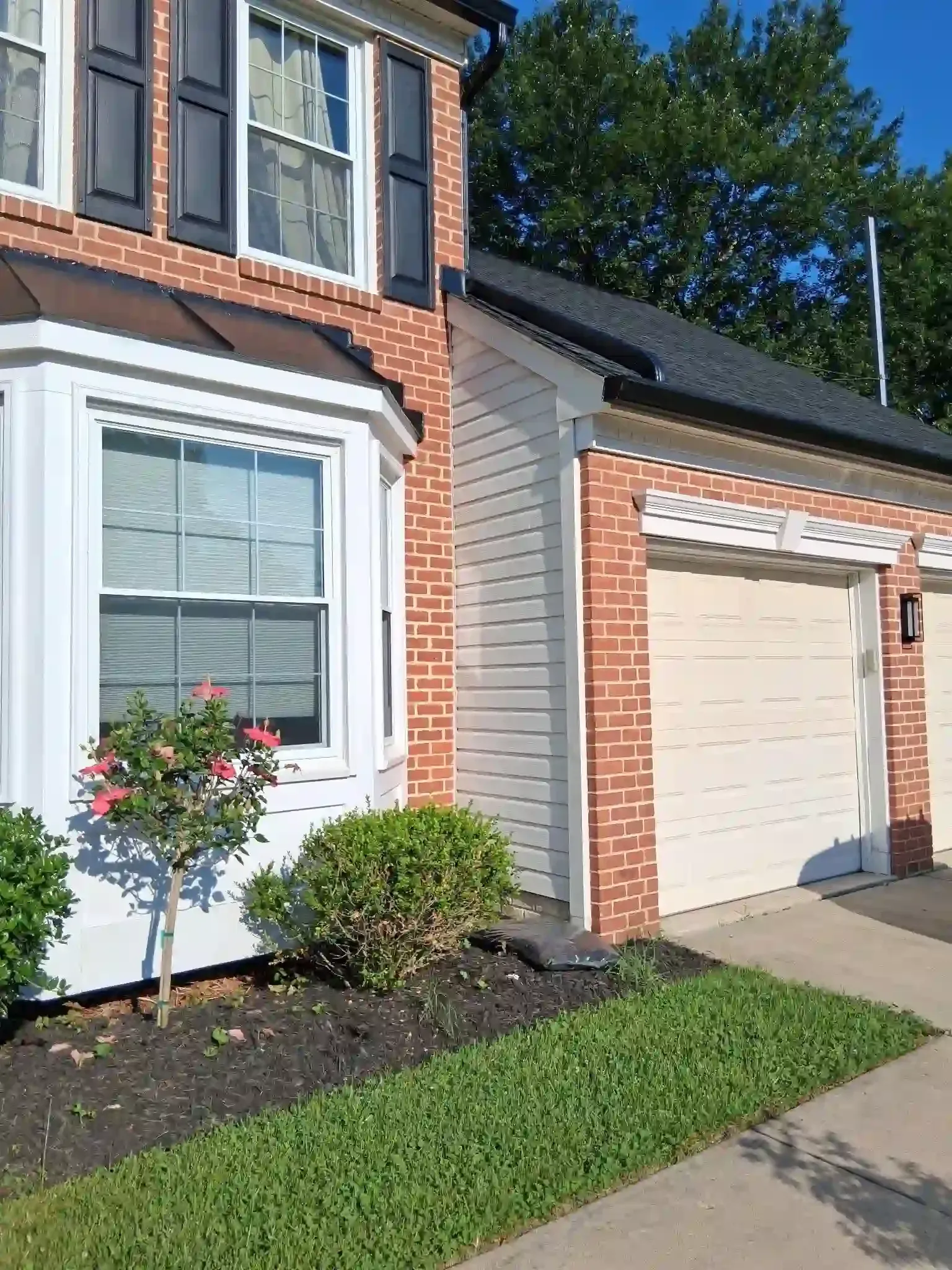 Brick house exterior with white trim, garage door, front window, and flowerbed beside a walkway
