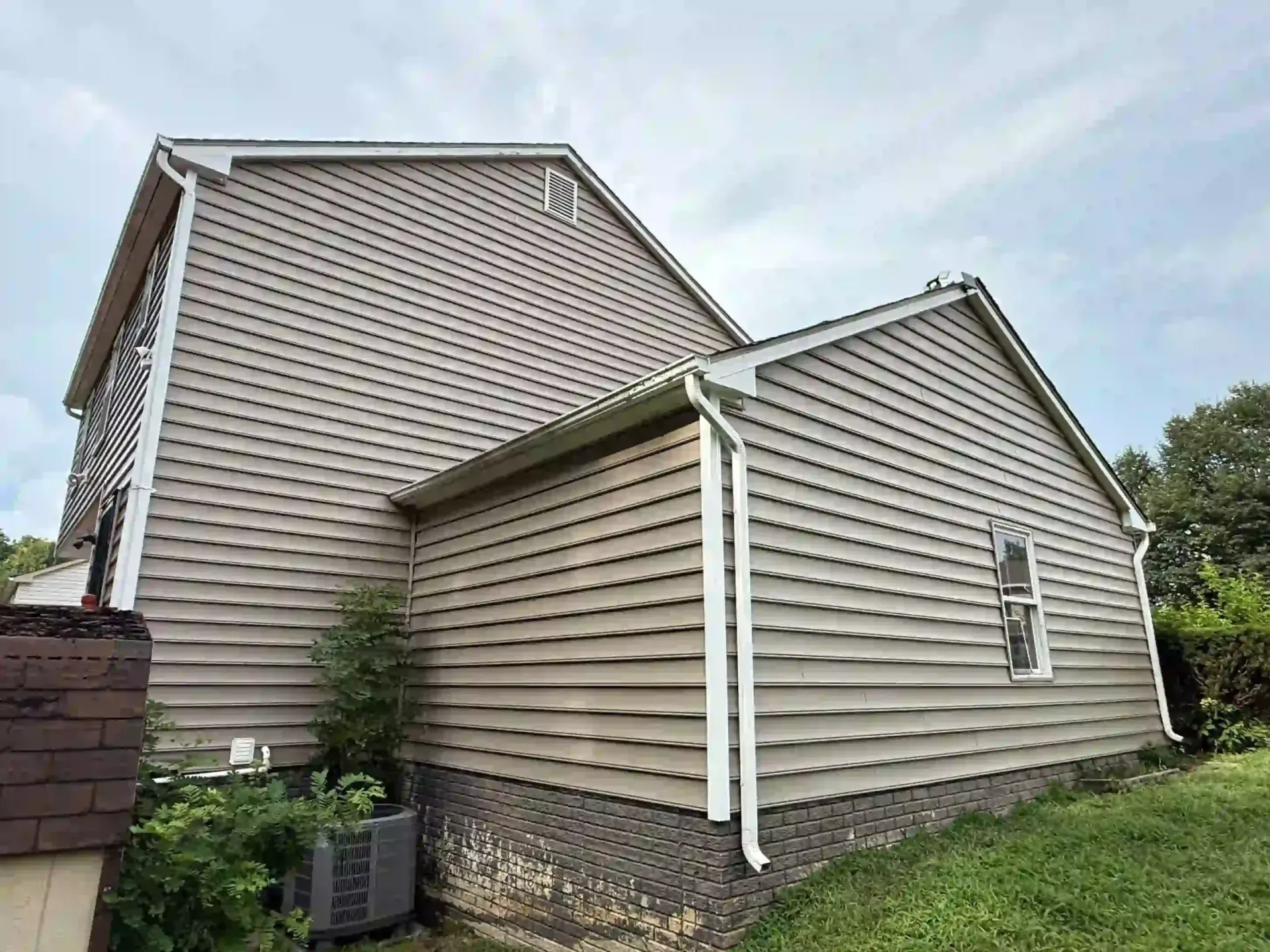 Two beige-sided house sections with white trim and stone foundation under a cloudy sky