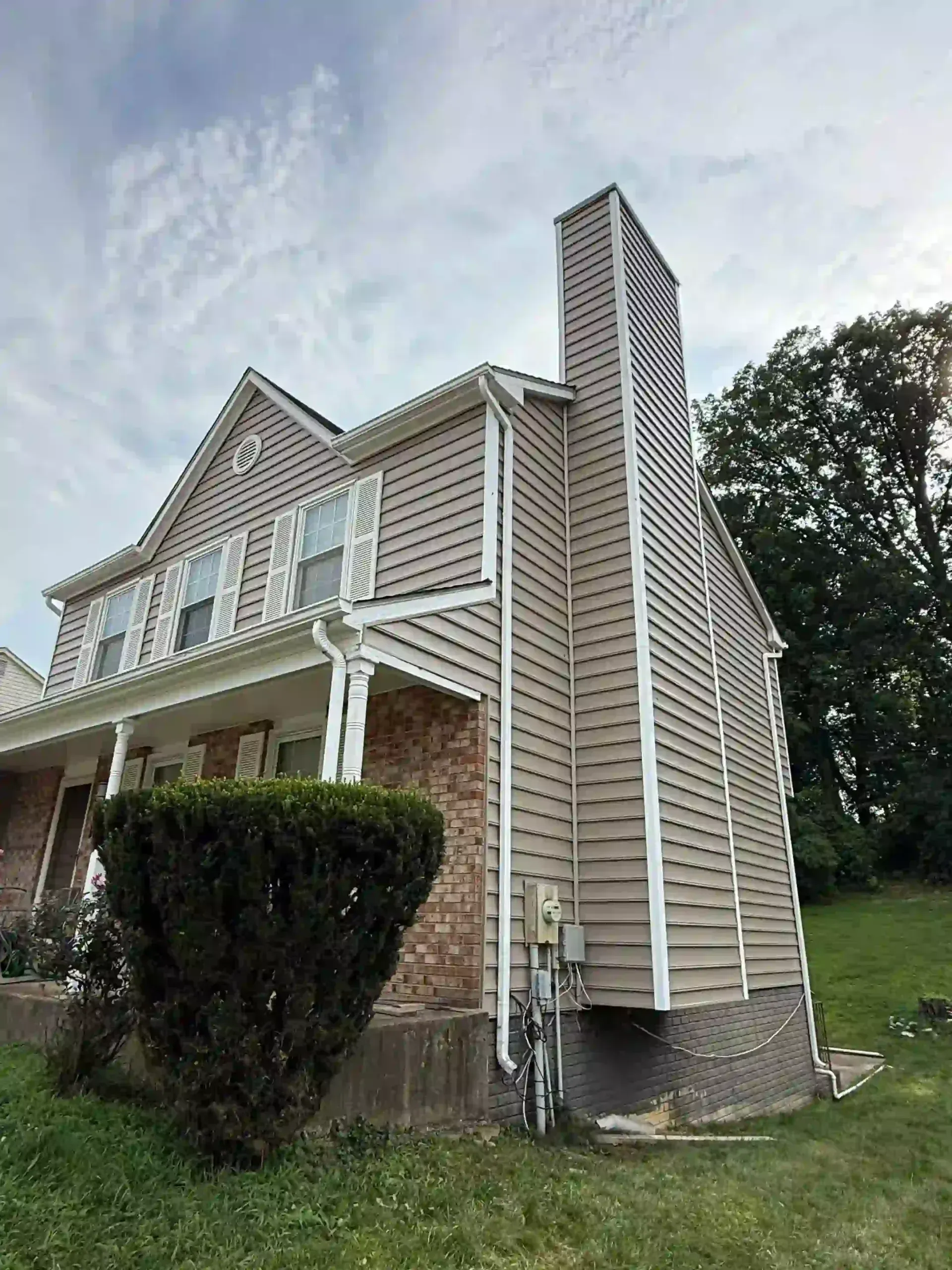 Suburban house exterior with brick porch, white siding, and tall chimney under a cloudy sky