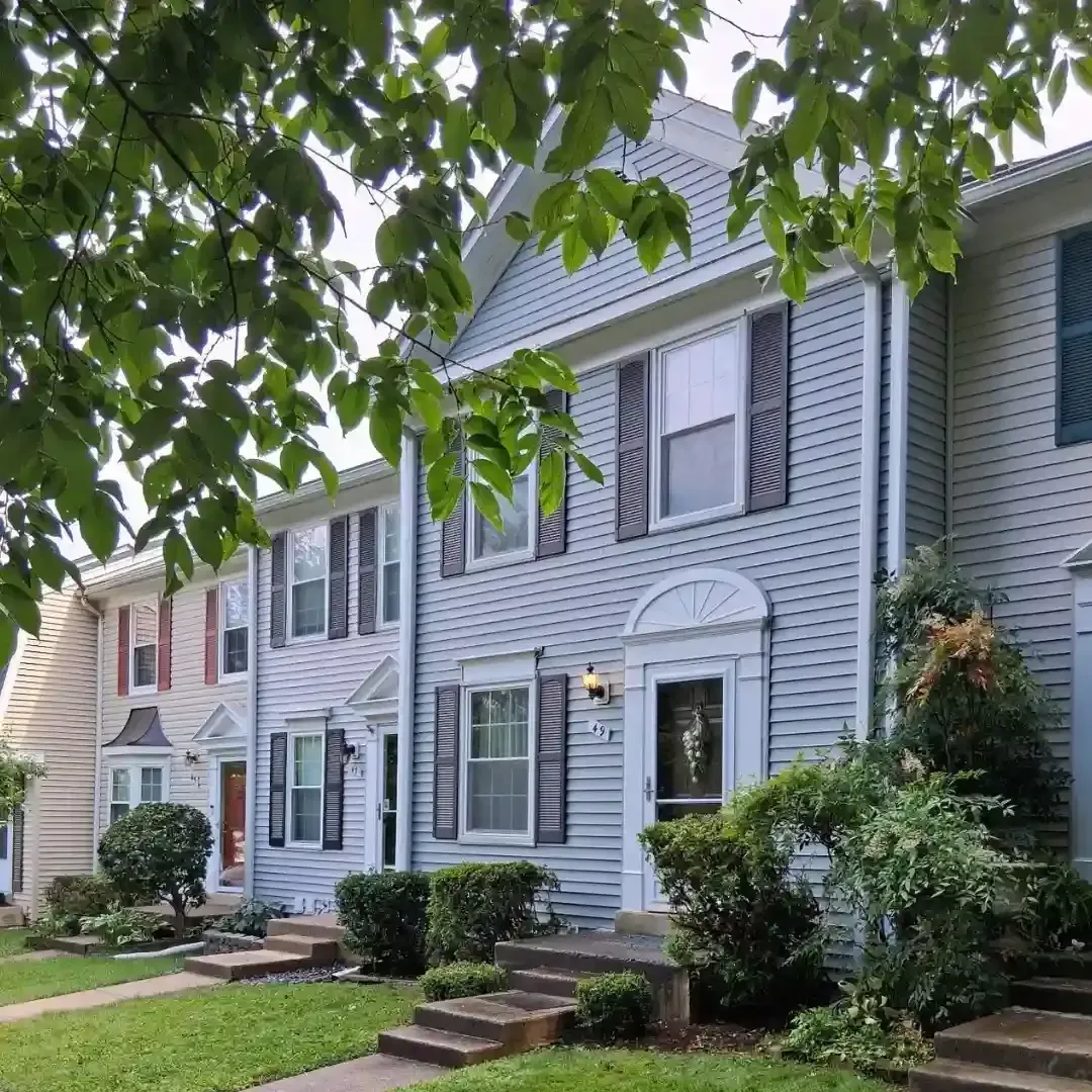 Row of blue-gray townhouses with white trim and front steps under leafy trees