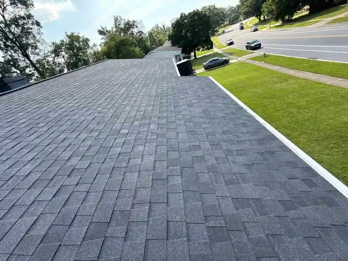 Gray shingle roof with white trim beside a green lawn and roadway