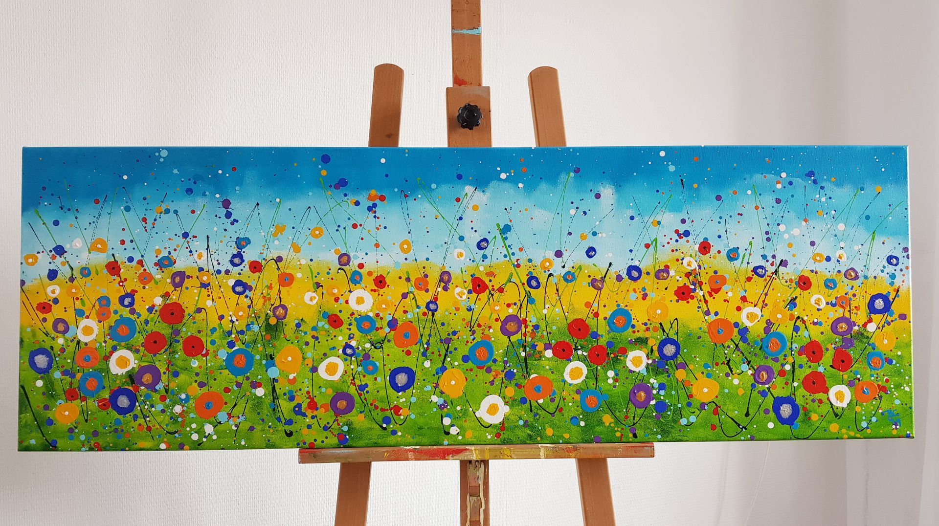 Kleurrijk schilderij van een veld met wilde bloemen op een canvas, op een houten ezel. Creatieve workshop.