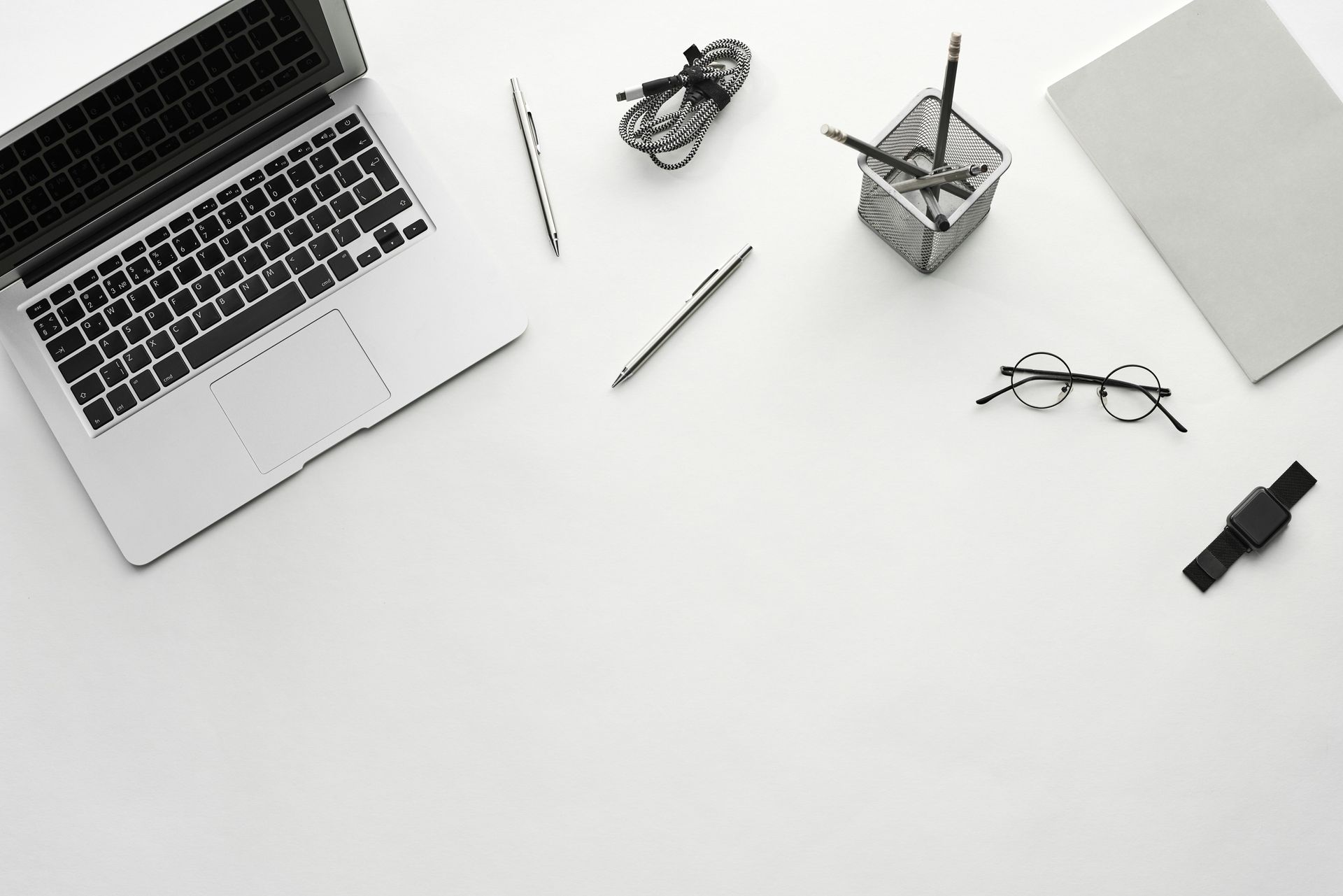Laptop en kantoorbenodigdheden op een wit oppervlak. Pennen, een bril, een horloge en een notitieboekje zijn ook aanwezig.