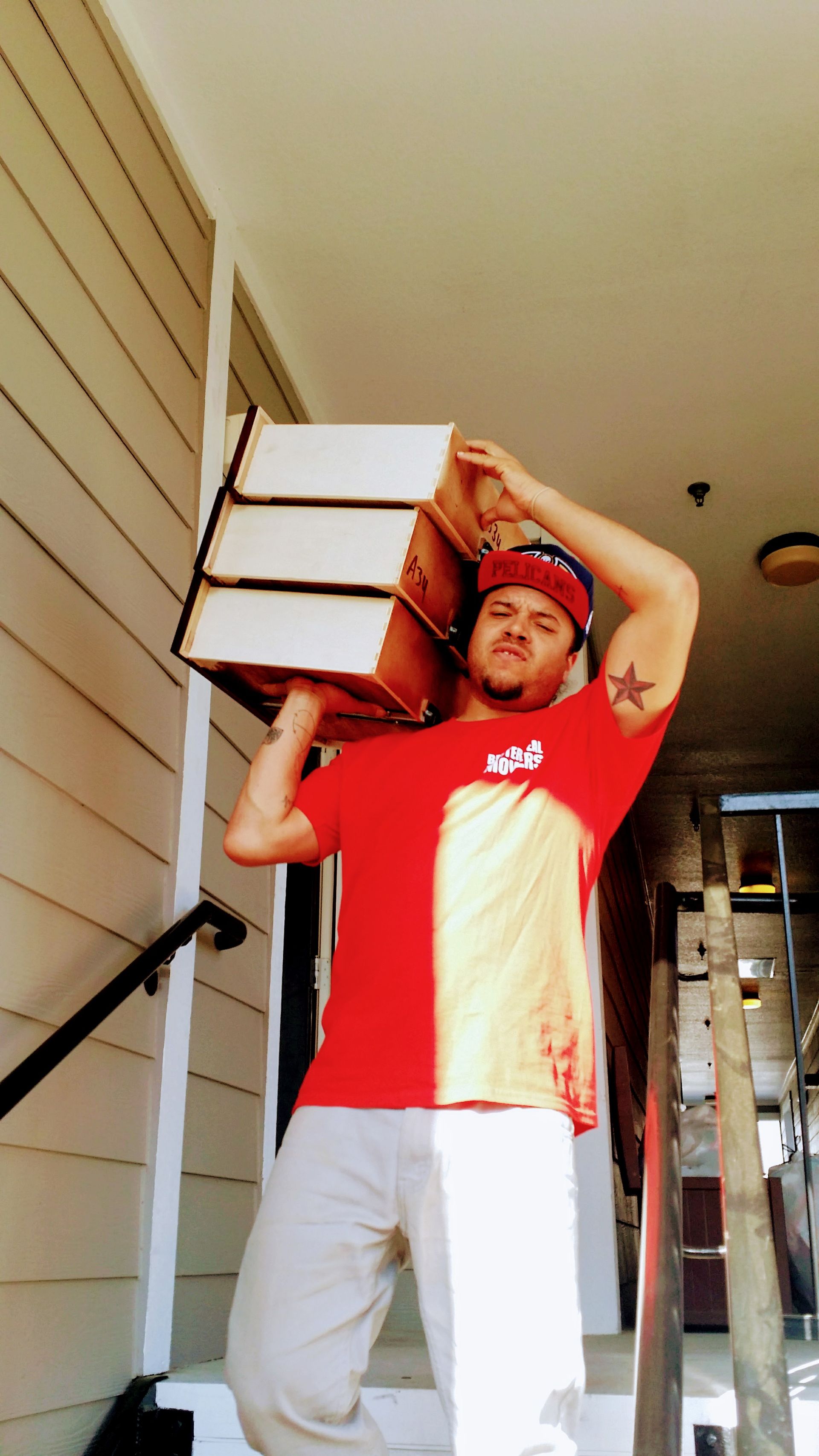 Man in red shirt carrying stacked boxes on his shoulder while walking up steps outdoors