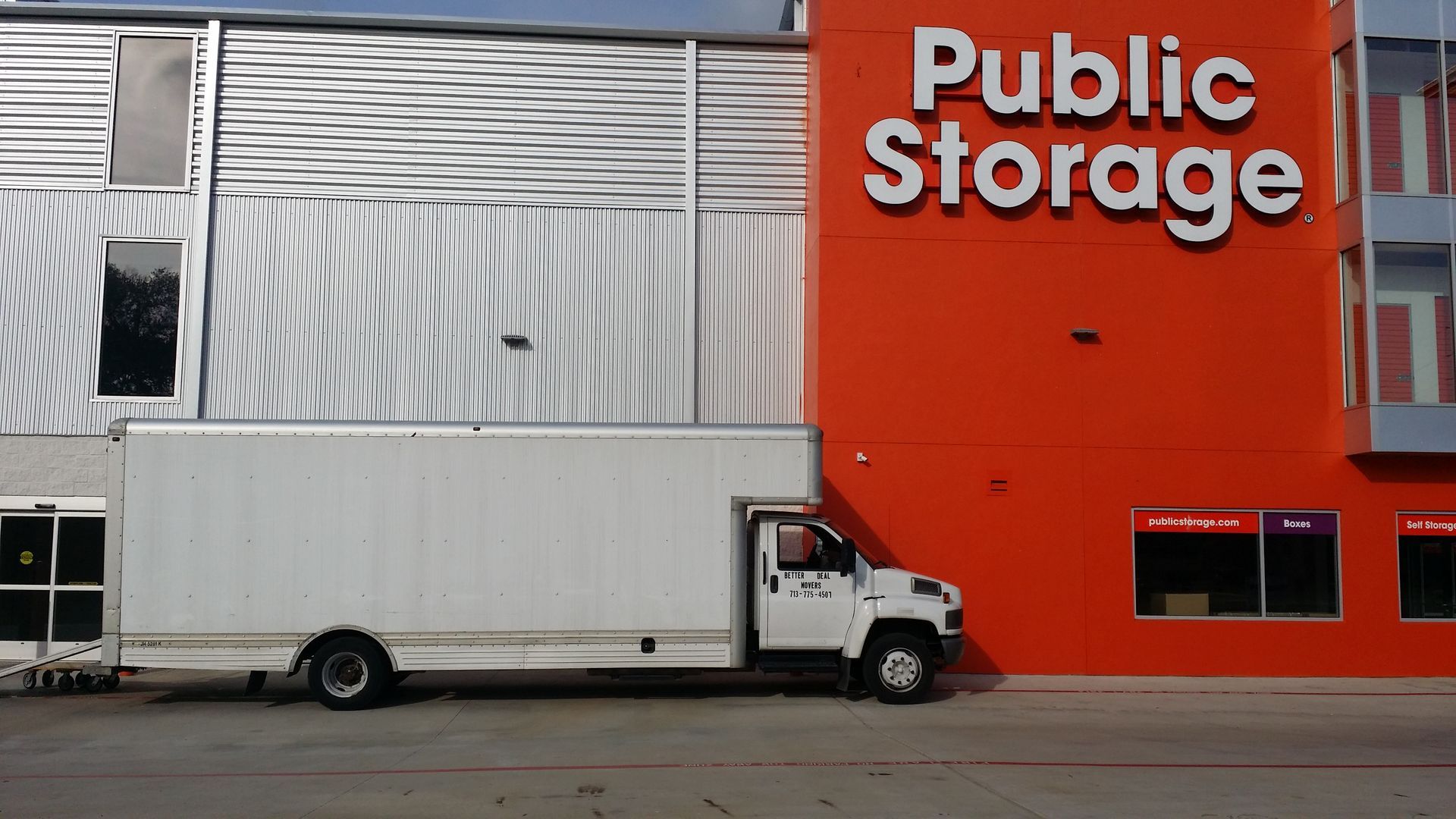 White box truck parked by a red Public Storage building with silver metal siding