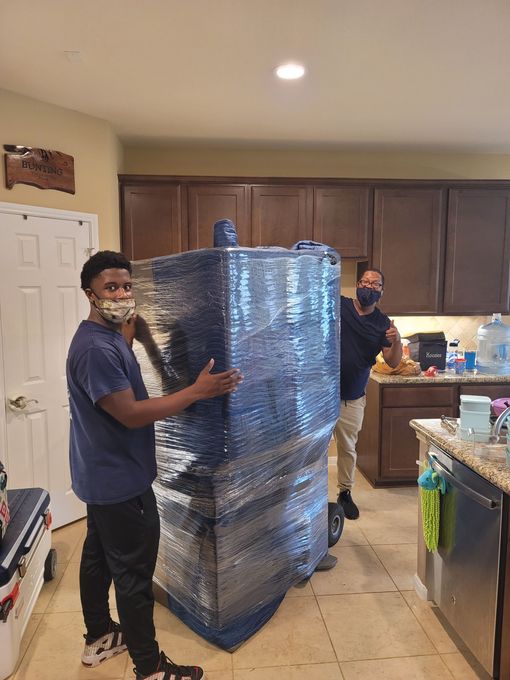 Two people moving a large shrink-wrapped pallet through a kitchen area