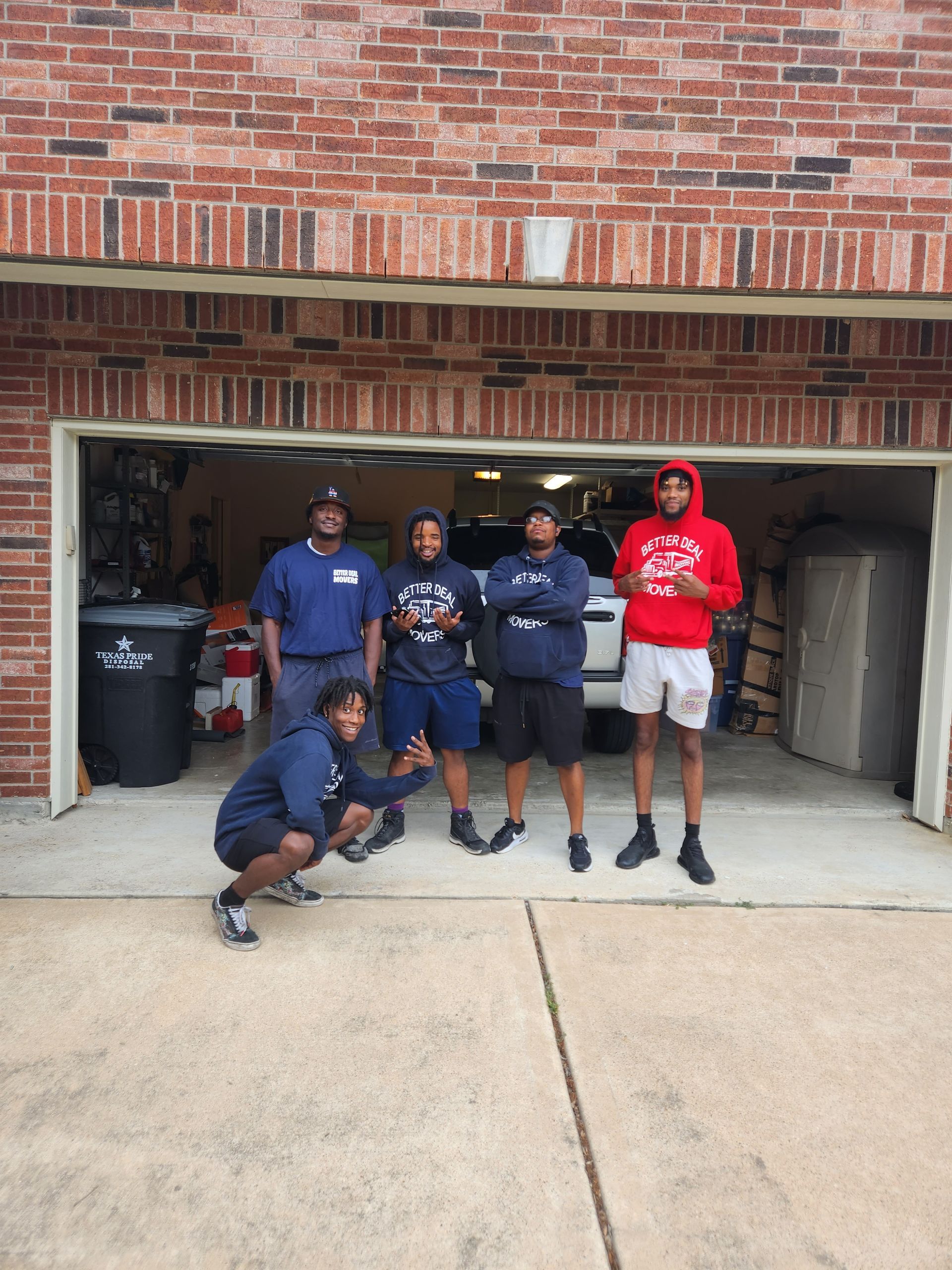 Five people pose in front of a brick garage, wearing navy and red shirts; one crouches in front.