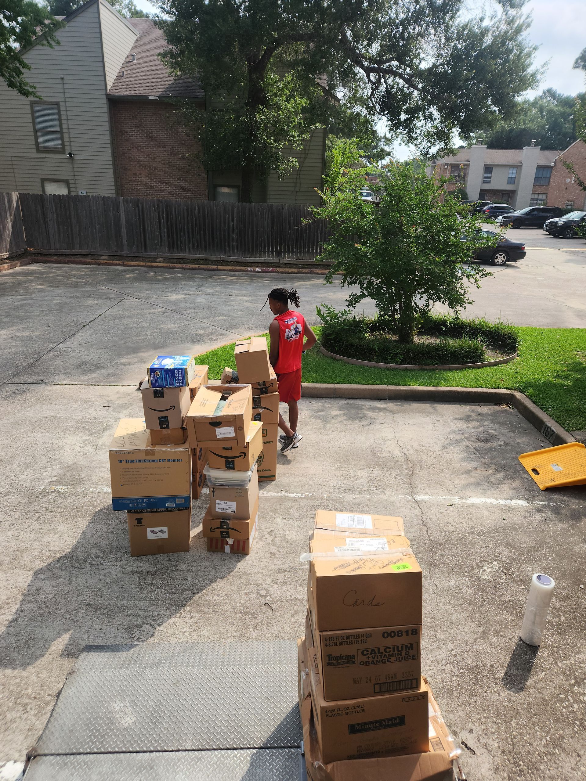 Child standing among stacked moving boxes in a residential parking lot near an apartment building.