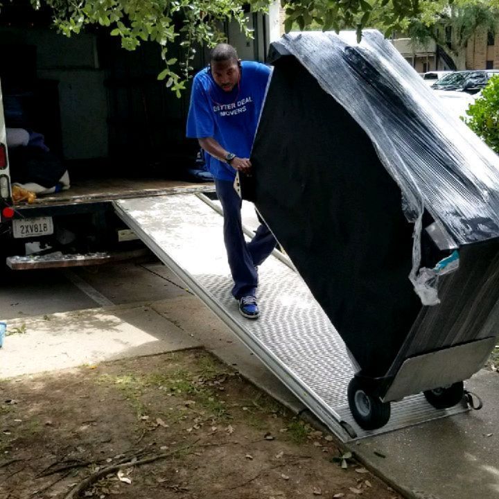 Person pushing a large black mattress on a dolly down a ramp from a truck