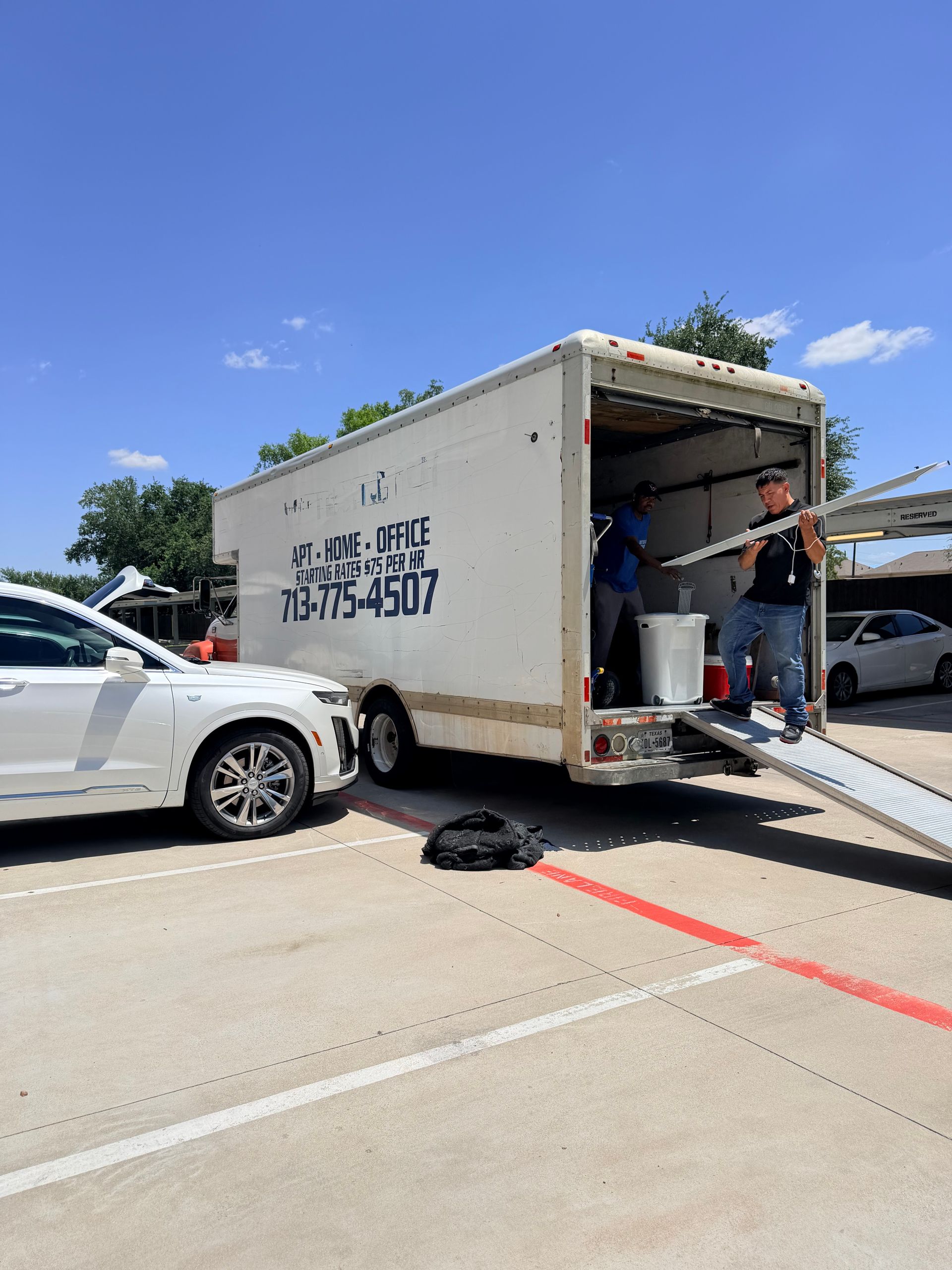 Tow truck loading a white sedan on a sunny roadside, with a worker at the rear of the truck.