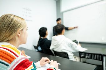 Students in a classroom watching a teacher point at a whiteboard