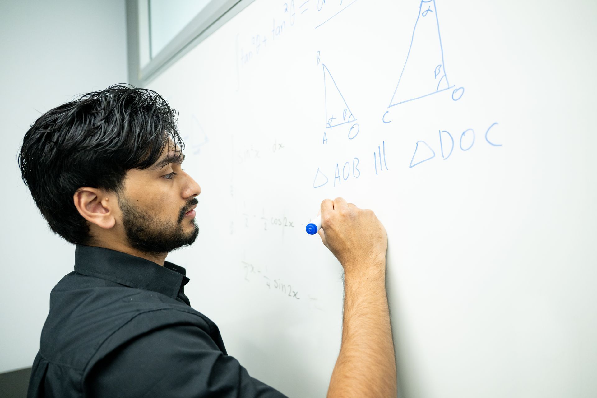 Person writing equations on a whiteboard in a classroom or office setting