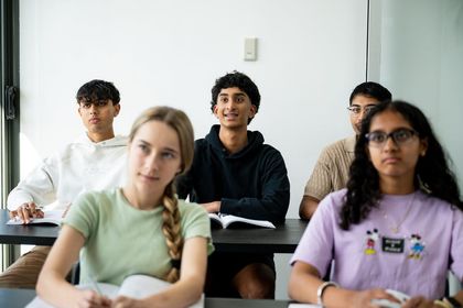Students seated in a classroom, facing forward with notebooks on desks