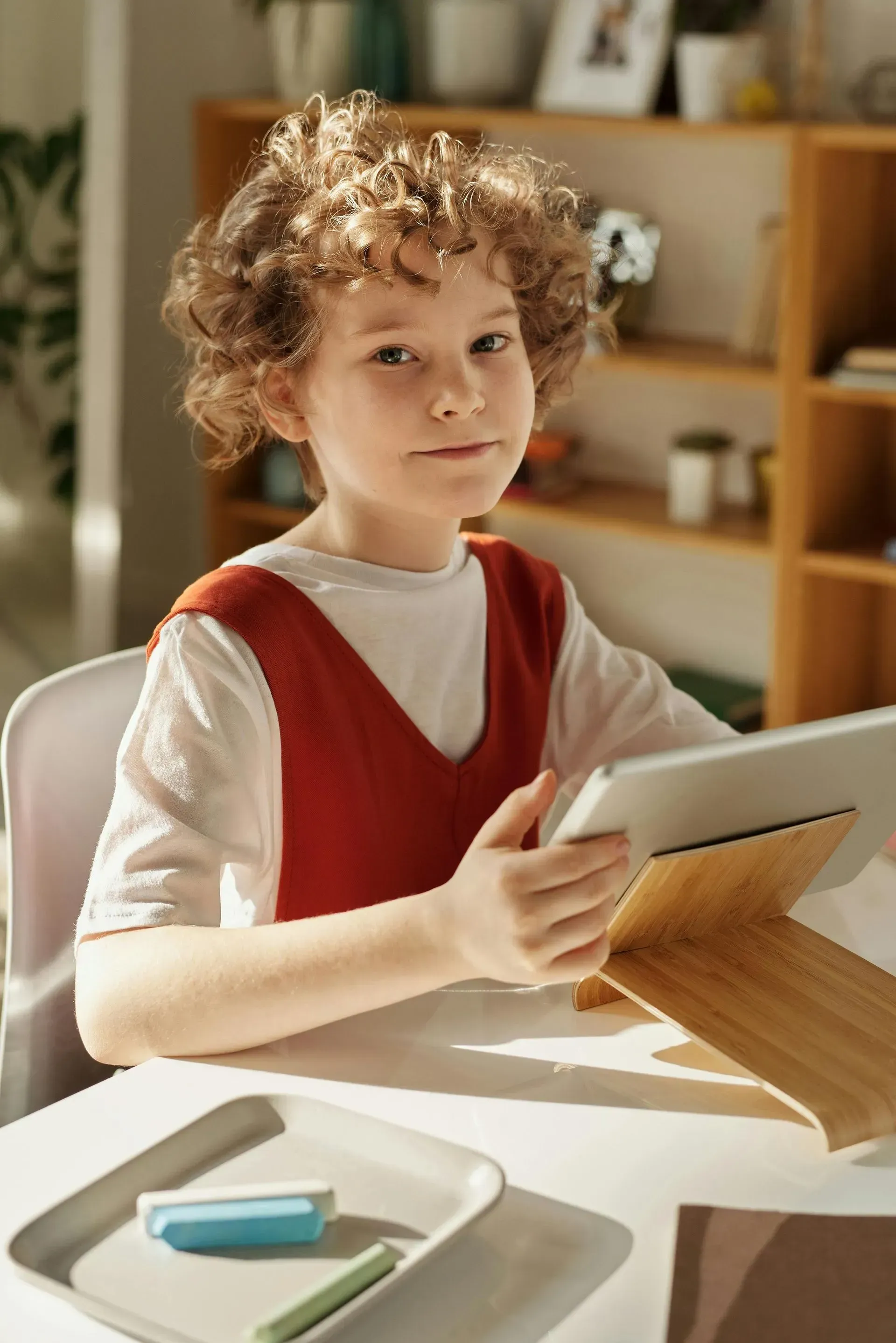 Two students study together at a table, writing in notebooks and reading a book.