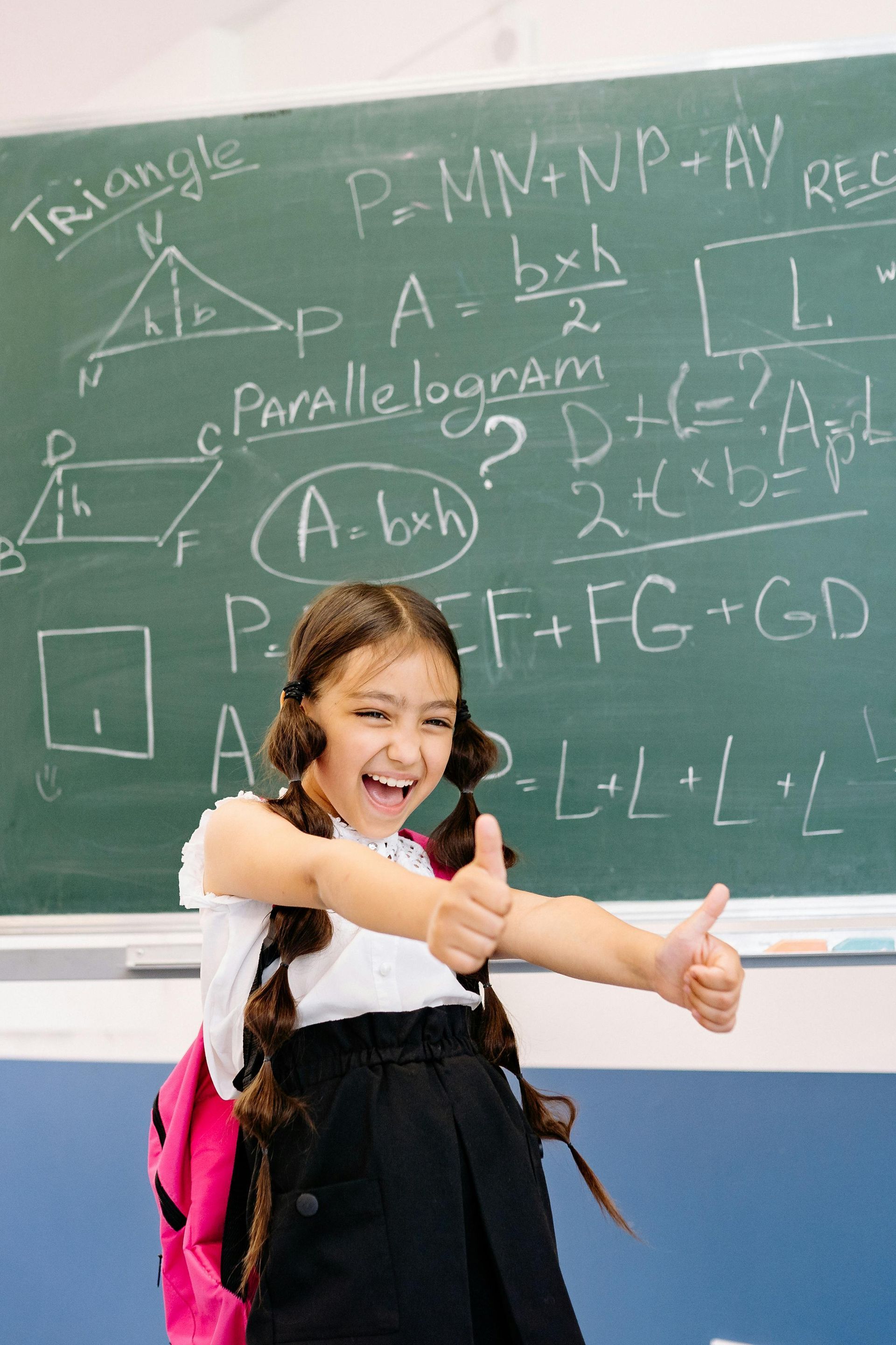 Smiling student giving two thumbs up in front of a chalkboard with math