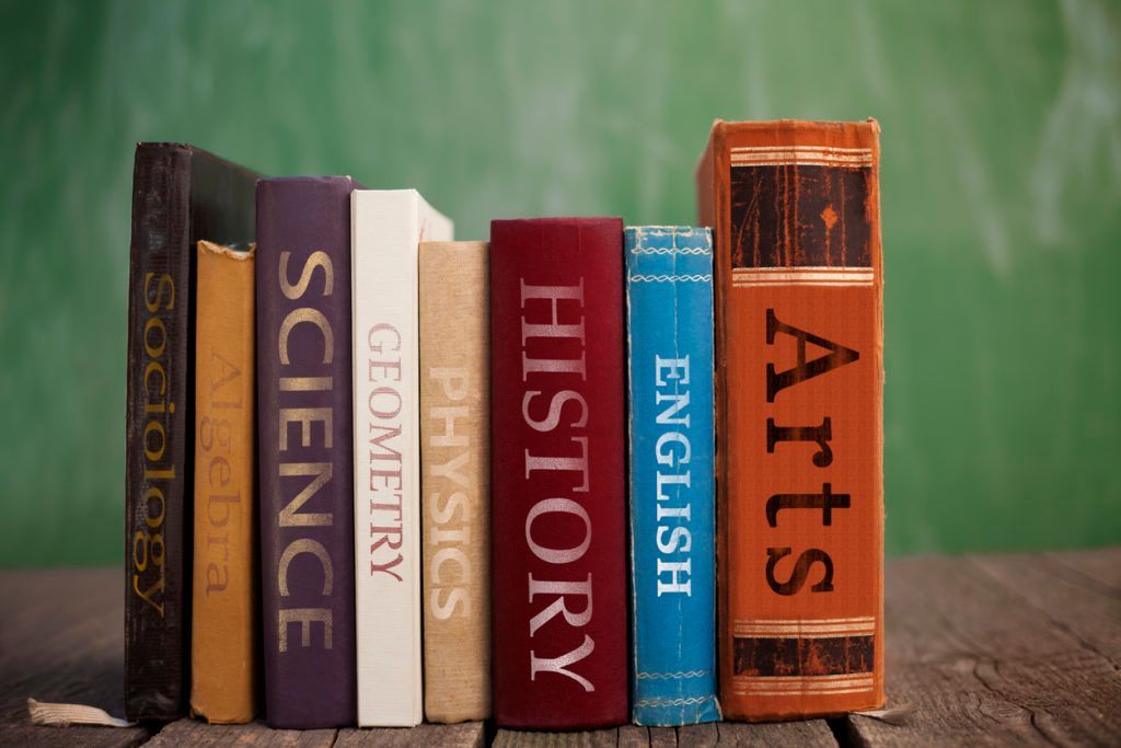 A row of eight colorful textbooks standing on a wooden surface against a green chalkboard background.